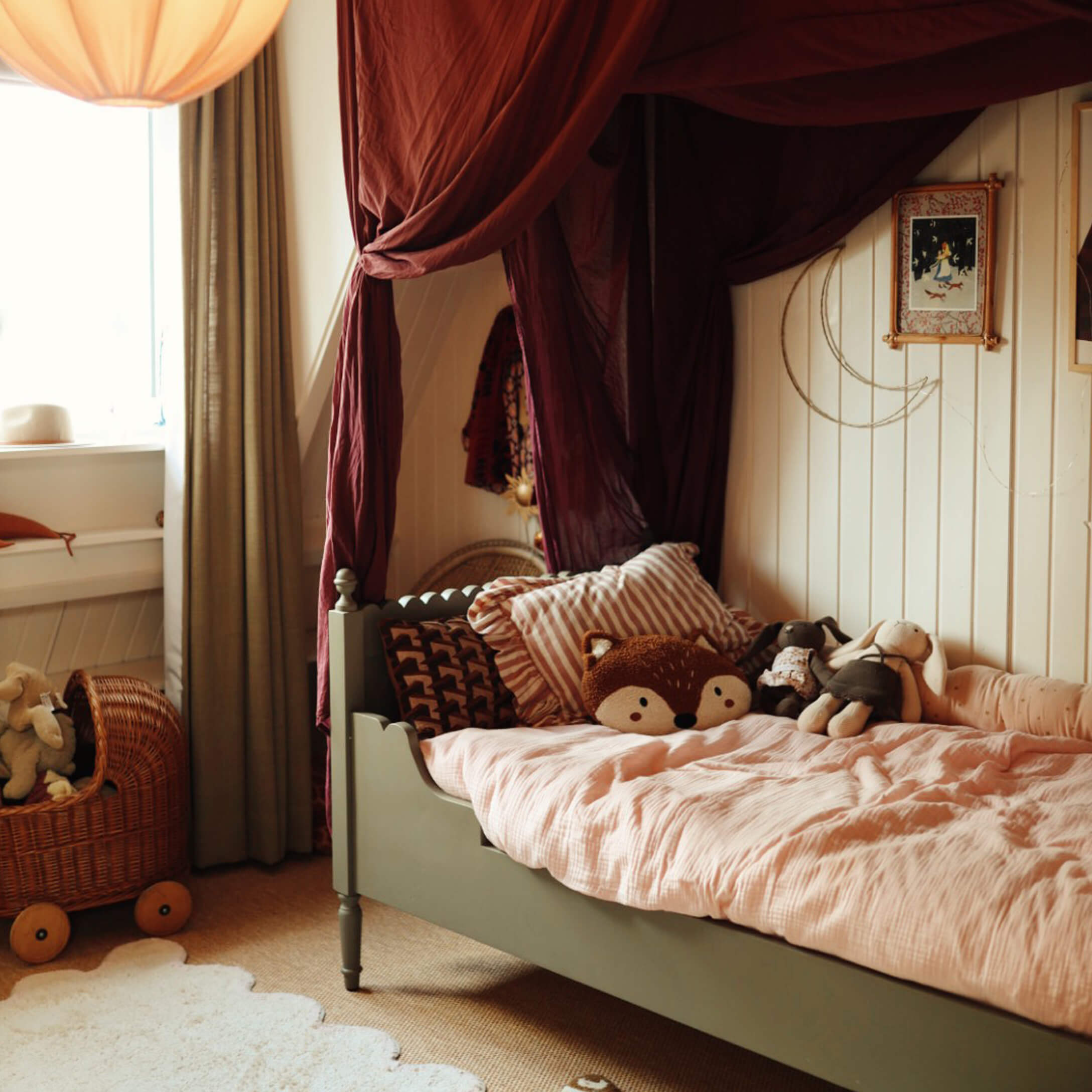 Gezellig kinderbed met groene lijst, roze beddengoed en knuffels in warme kamer met bordeaux gordijnen