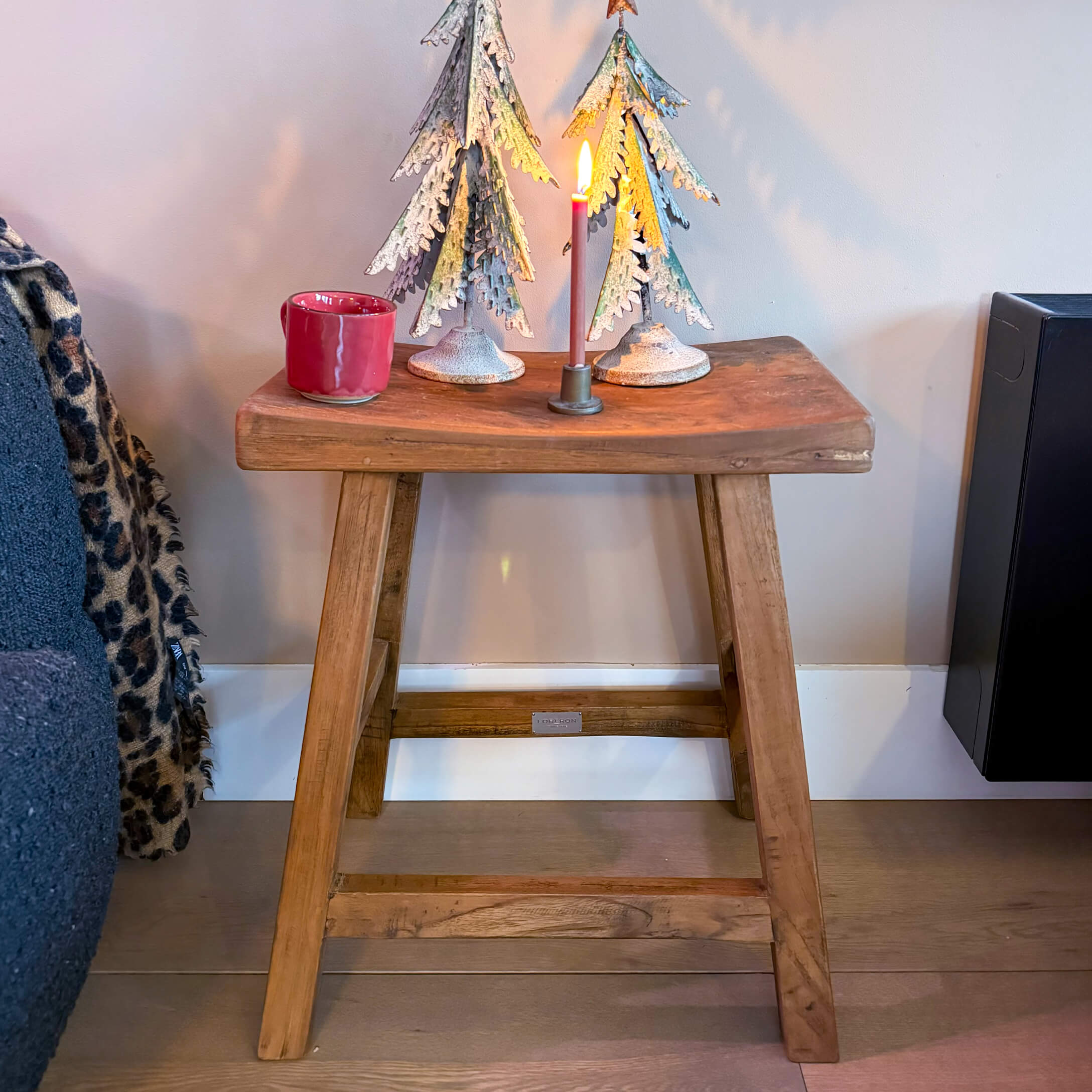 Houten kruk met metalen kerstbomen en brandende kaars in industriële stijl op het blad