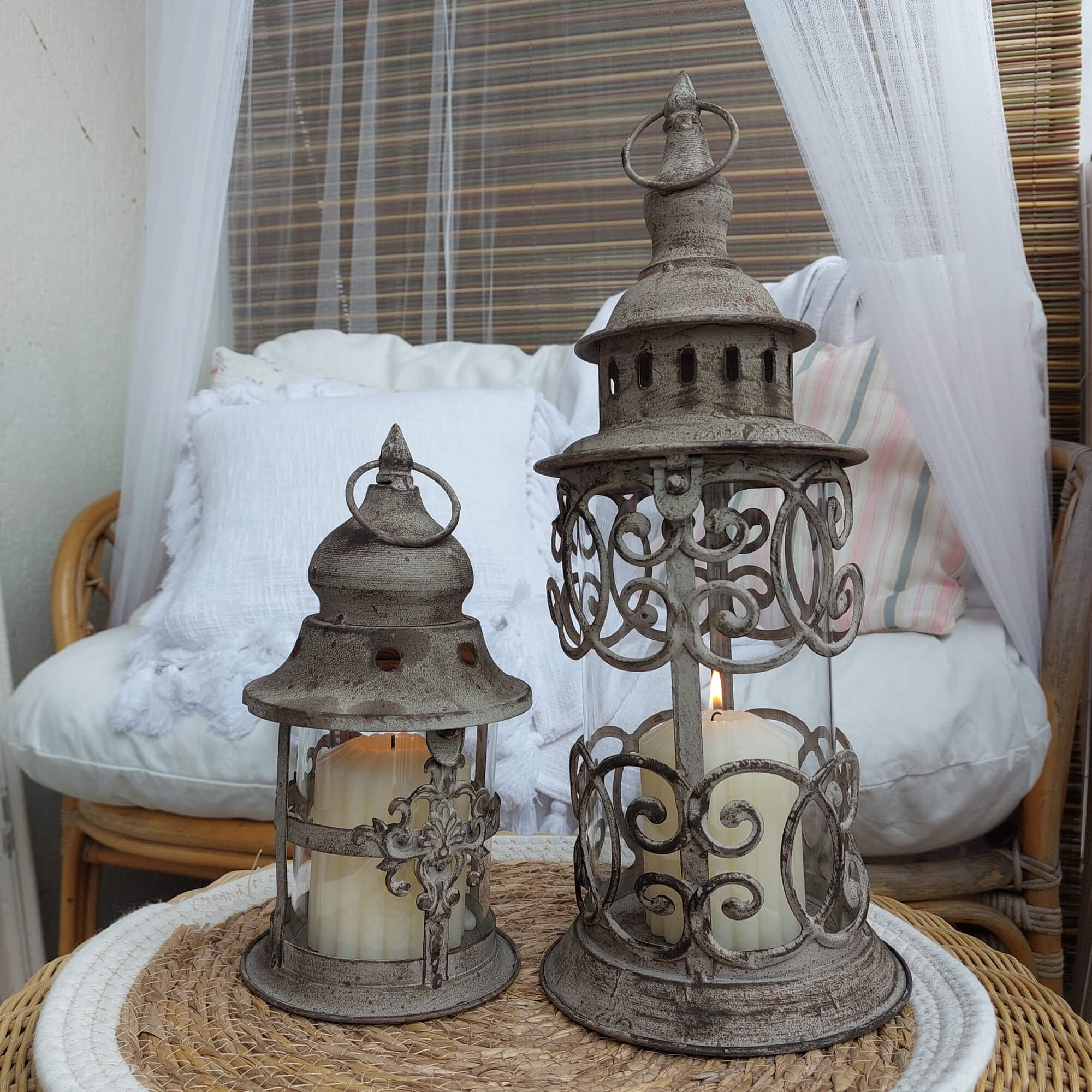 Twee decoratieve vintage metalen lantaarns in grijs met witte kaarsen op een rotan tafel