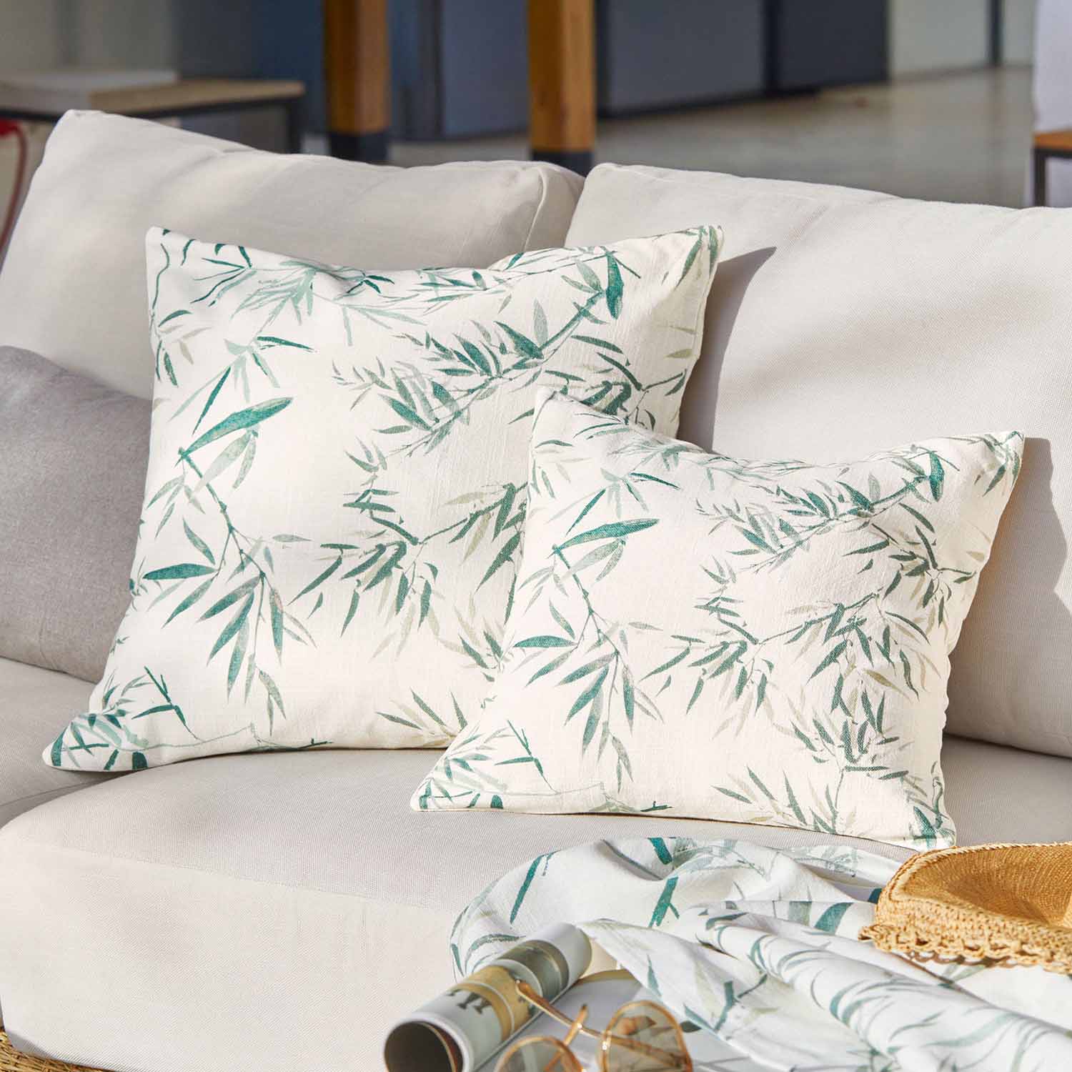 Twee decoratieve katoenen kussens in crèmekleur met groen bladmotief op een lichte bank