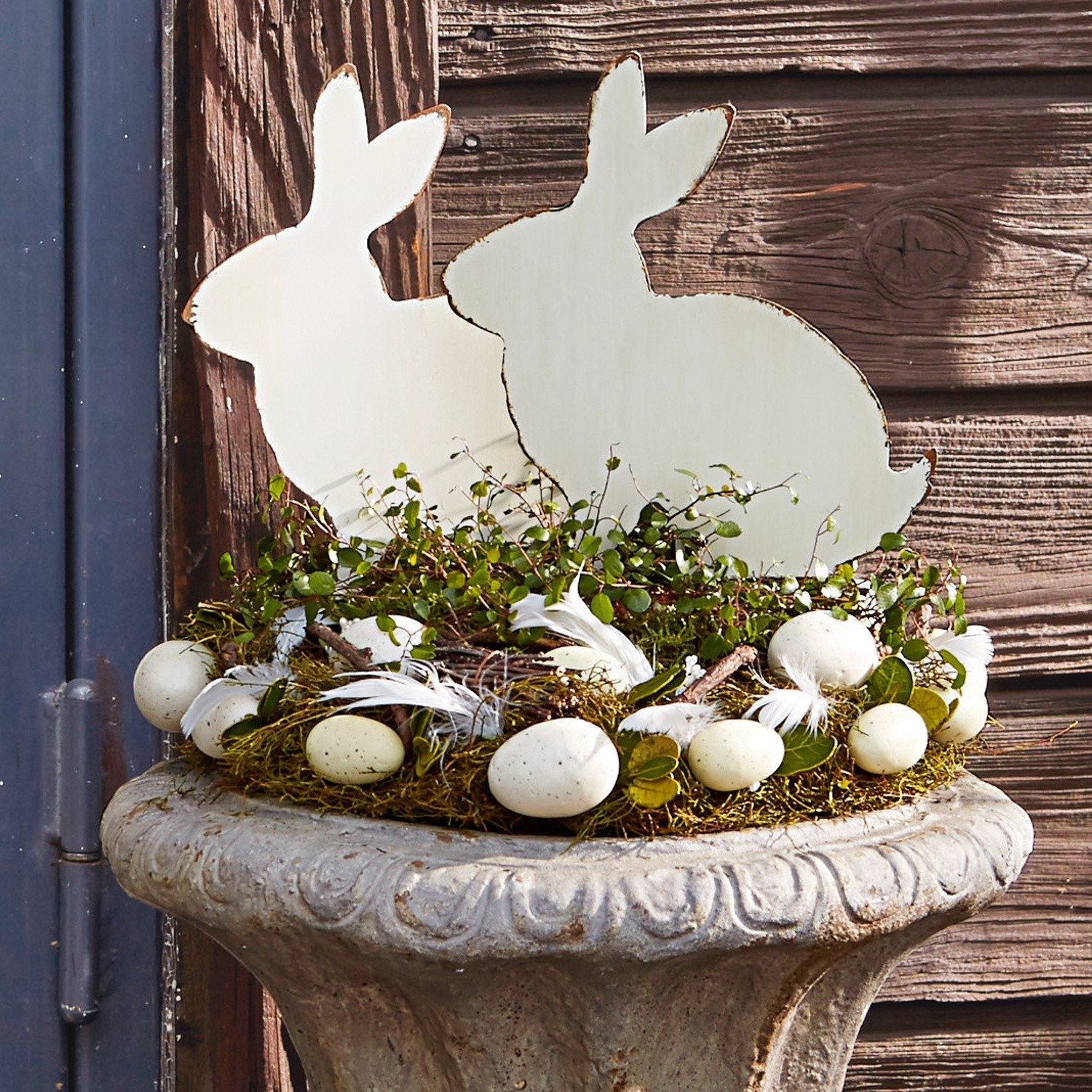 Paasdecoratie met witte houten konijnen en eieren op mos in stenen pot