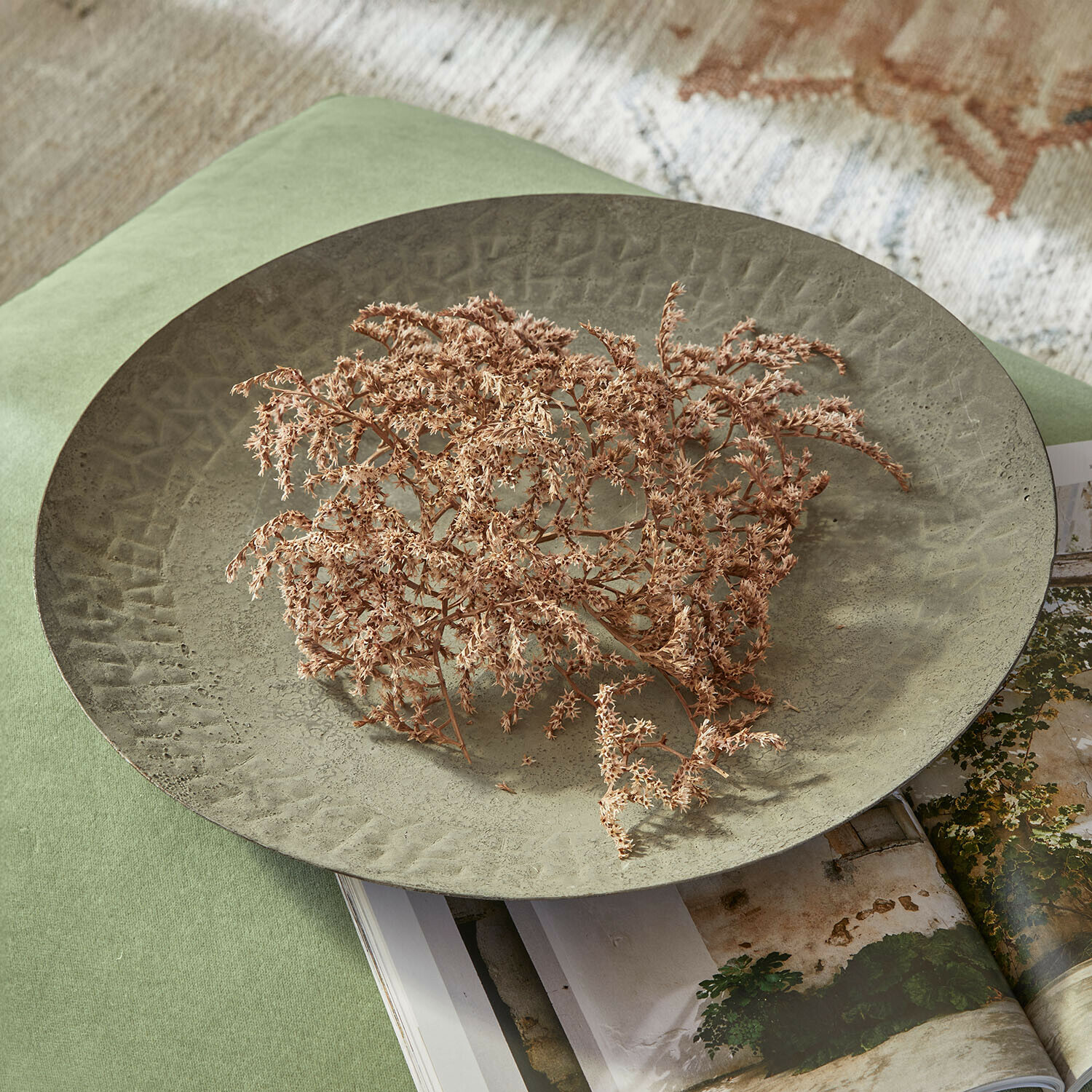 Grote groene metalen decoratieve schaal met textuur en gedroogde bloemen op groene stof en tijdschrift