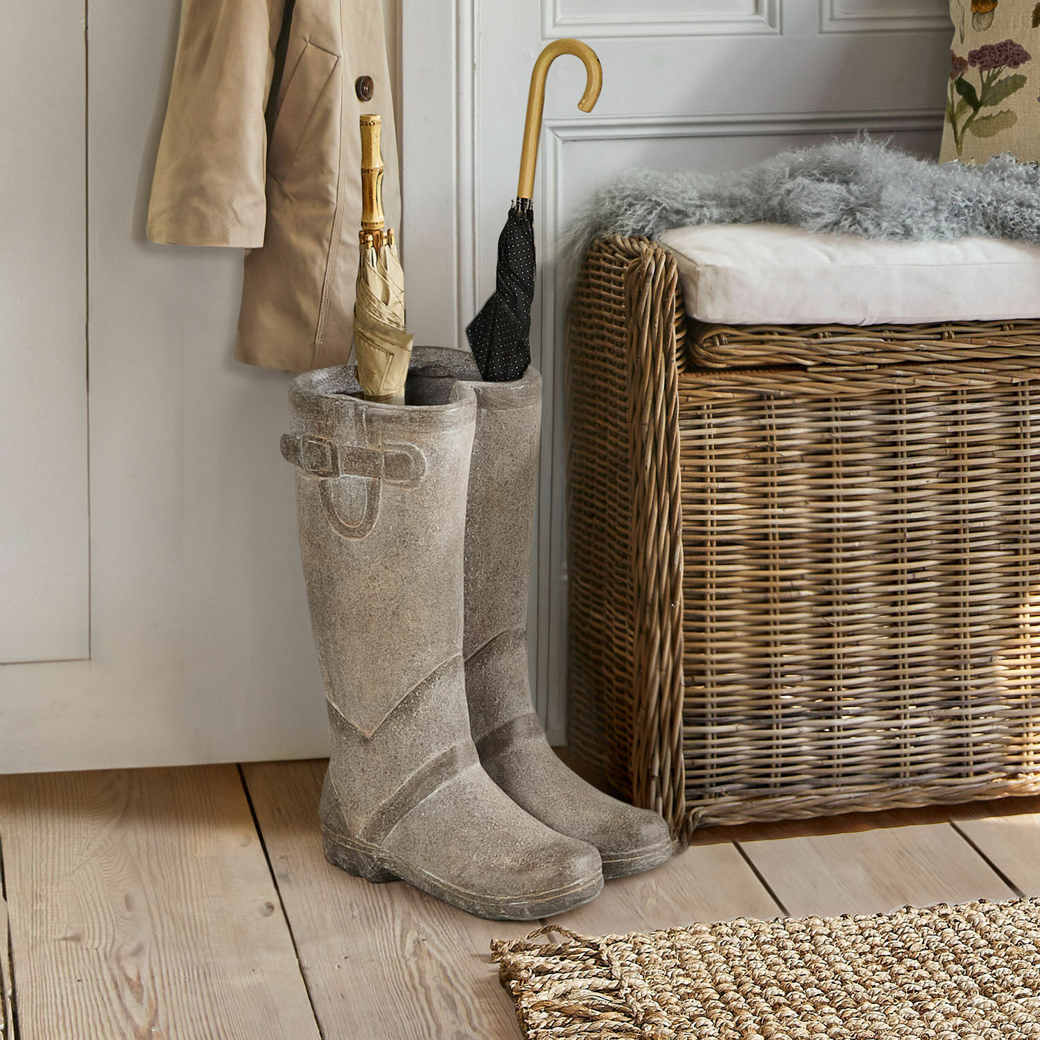 Grijze rubberen laarzen bij de deur met paraplu's en een rieten bankje ernaast