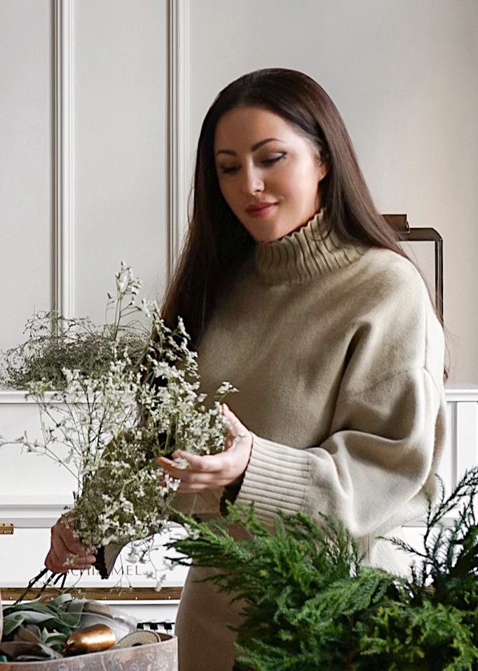 Vrouw in beige coltrui die delicate witte bloemen vasthoudt in lichte kamer