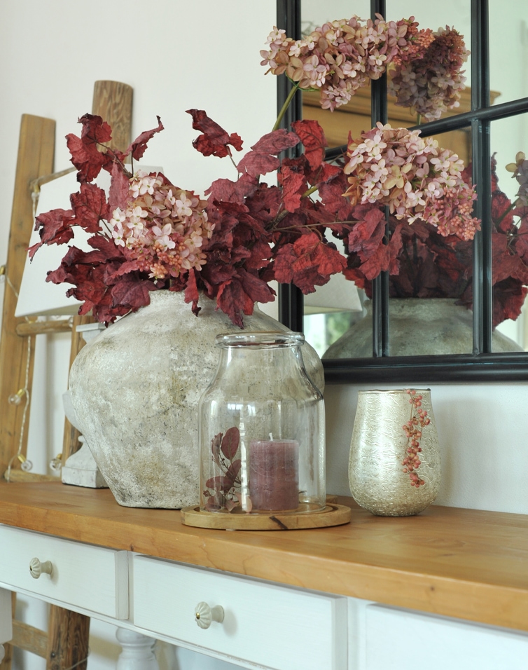 Decoratieve stenen vaas met rode bladeren en roze bloemen op houten tafel in woonkamer