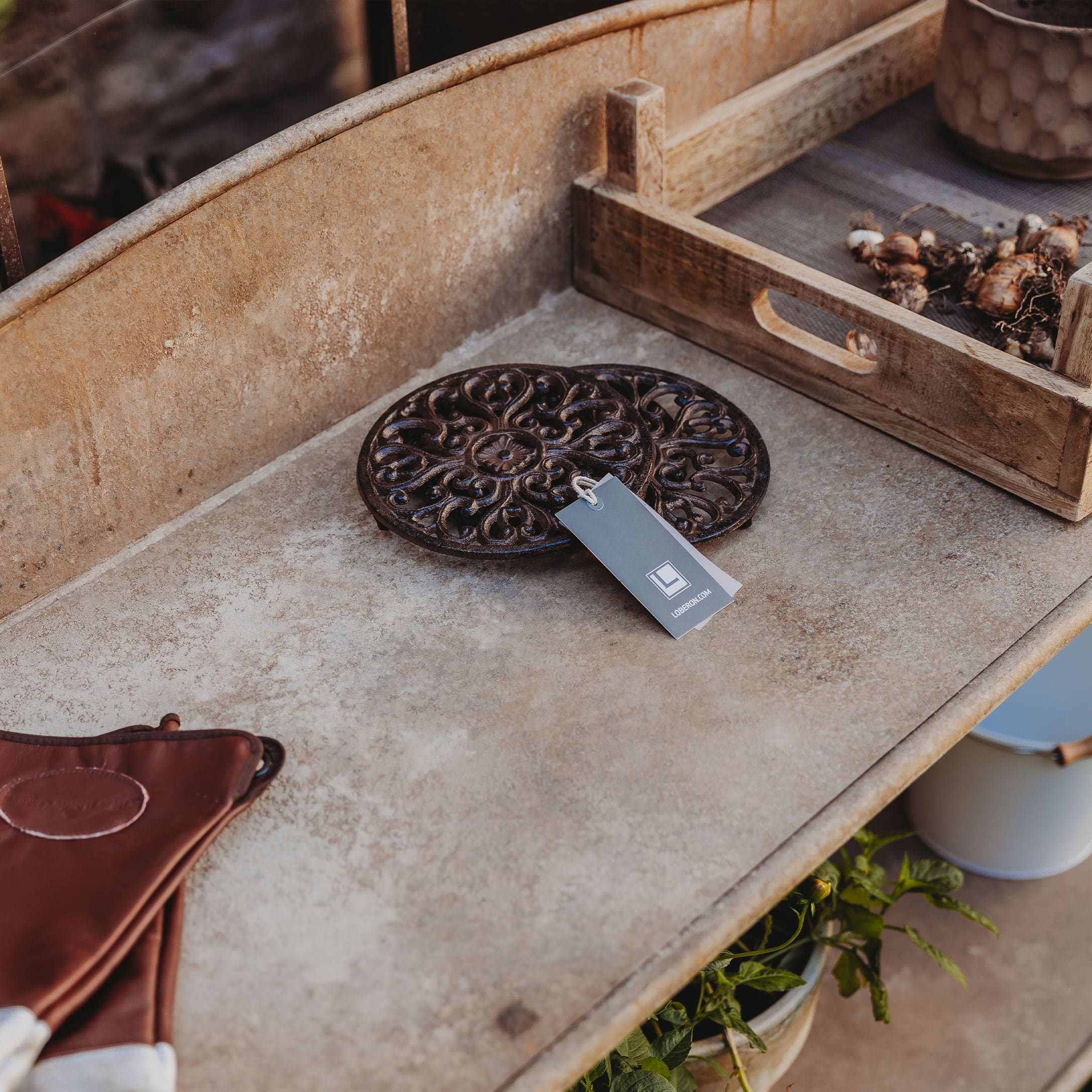 Ronde decoratieve onderzetter van donker metaal op rustieke tuintafel