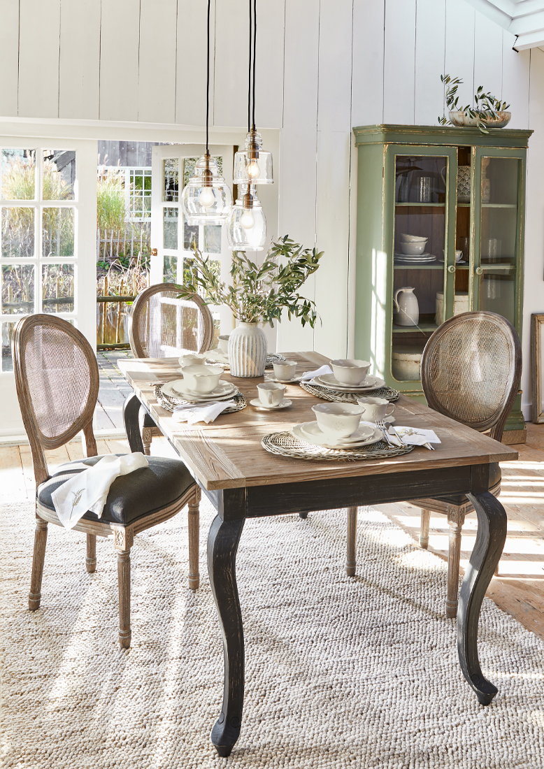 Eetkamer met houten tafel en vintage rieten stoelen, natuurlijk licht en stijlvolle decoratie