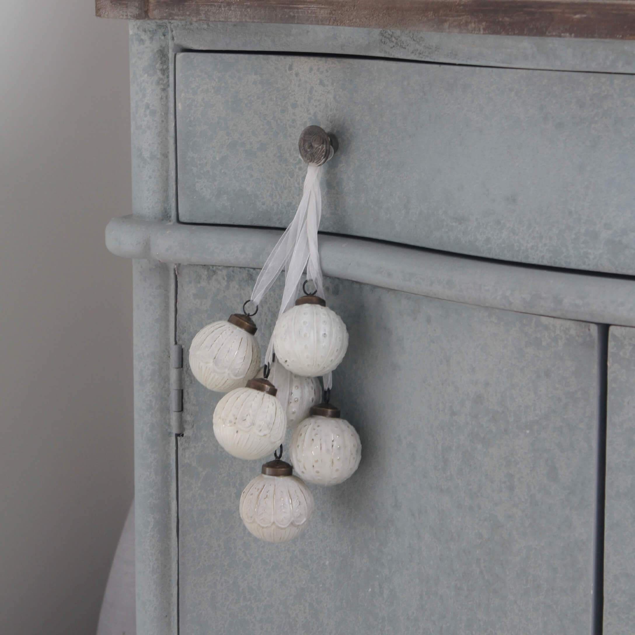 Set witte decoratieve ballen met fijn patroon hangend aan grijs metalen meubel