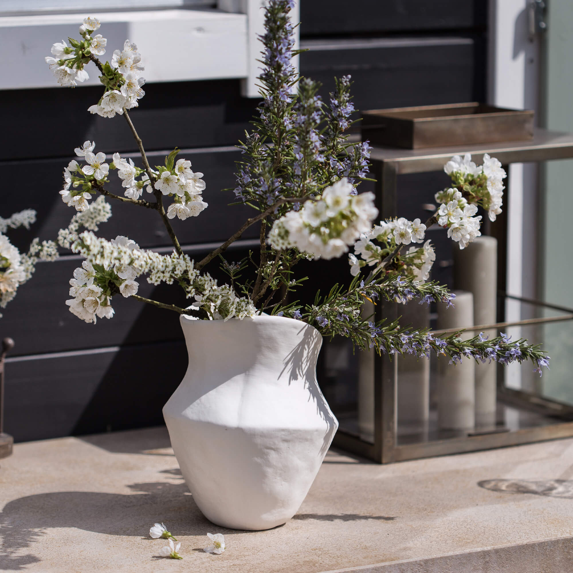 Witte keramische vaas met bloemen en takken op decoratieve buitentafel