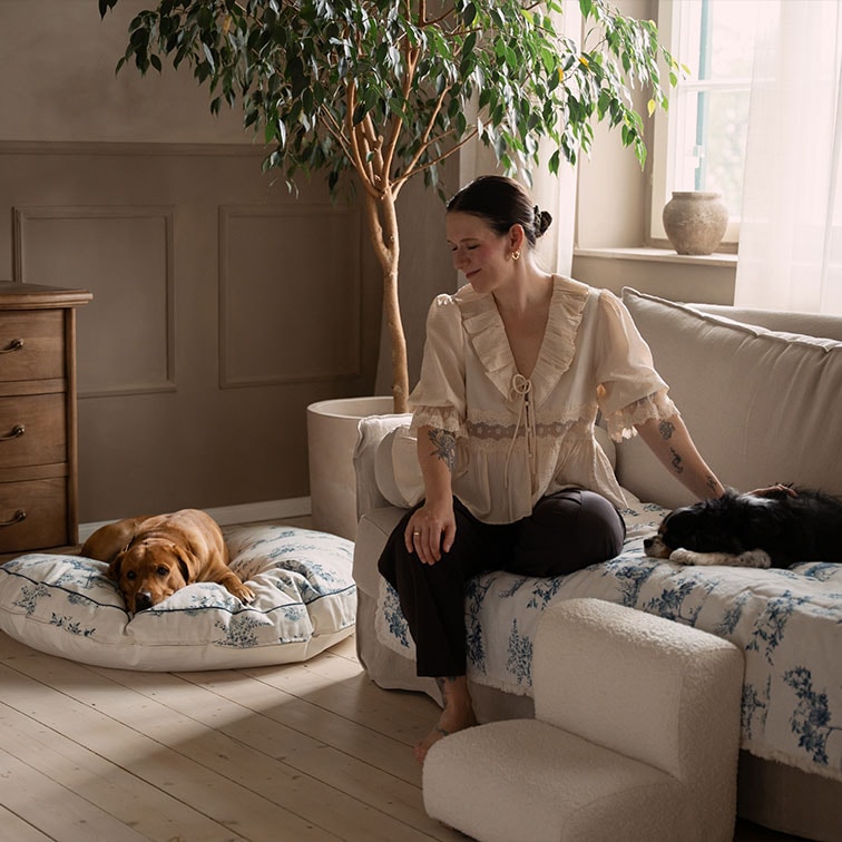 Vrouw in beige blouse zittend op bank met twee honden in een gezellige, lichte woonkamer