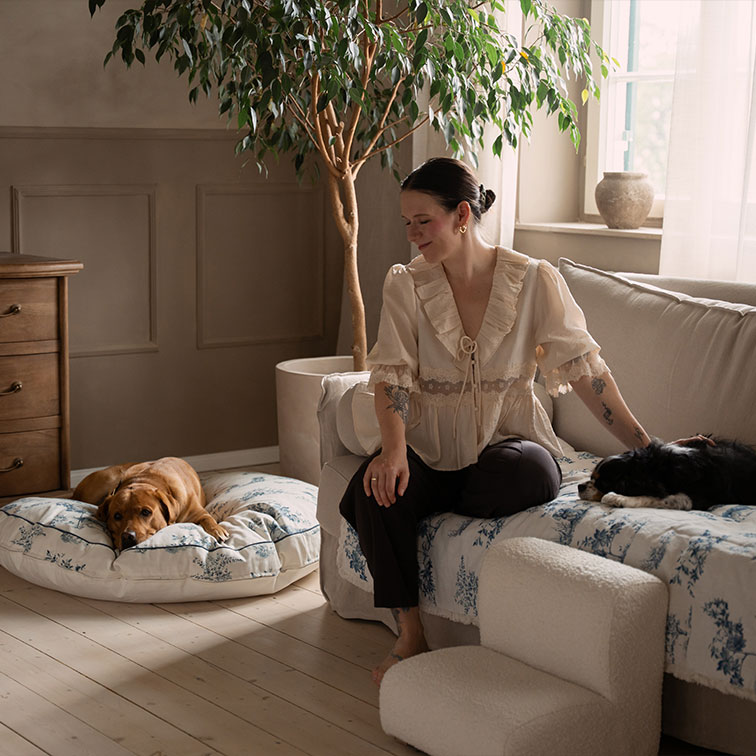 Vrouw in beige blouse zittend op bank met twee honden in een gezellige, lichte woonkamer