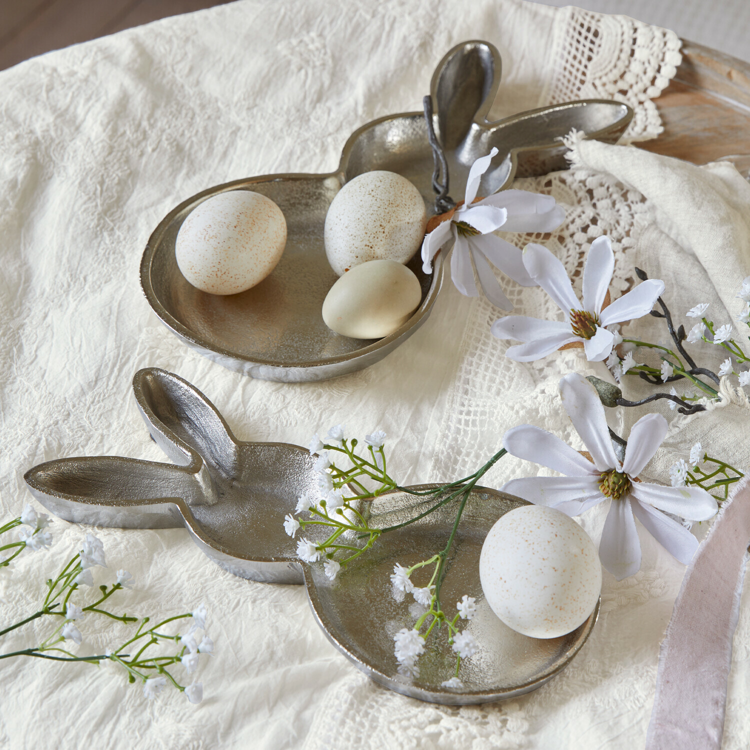 Metalen dienblad in konijnenvorm met witte eieren en bloemen op lichte doek, paasdecoratie