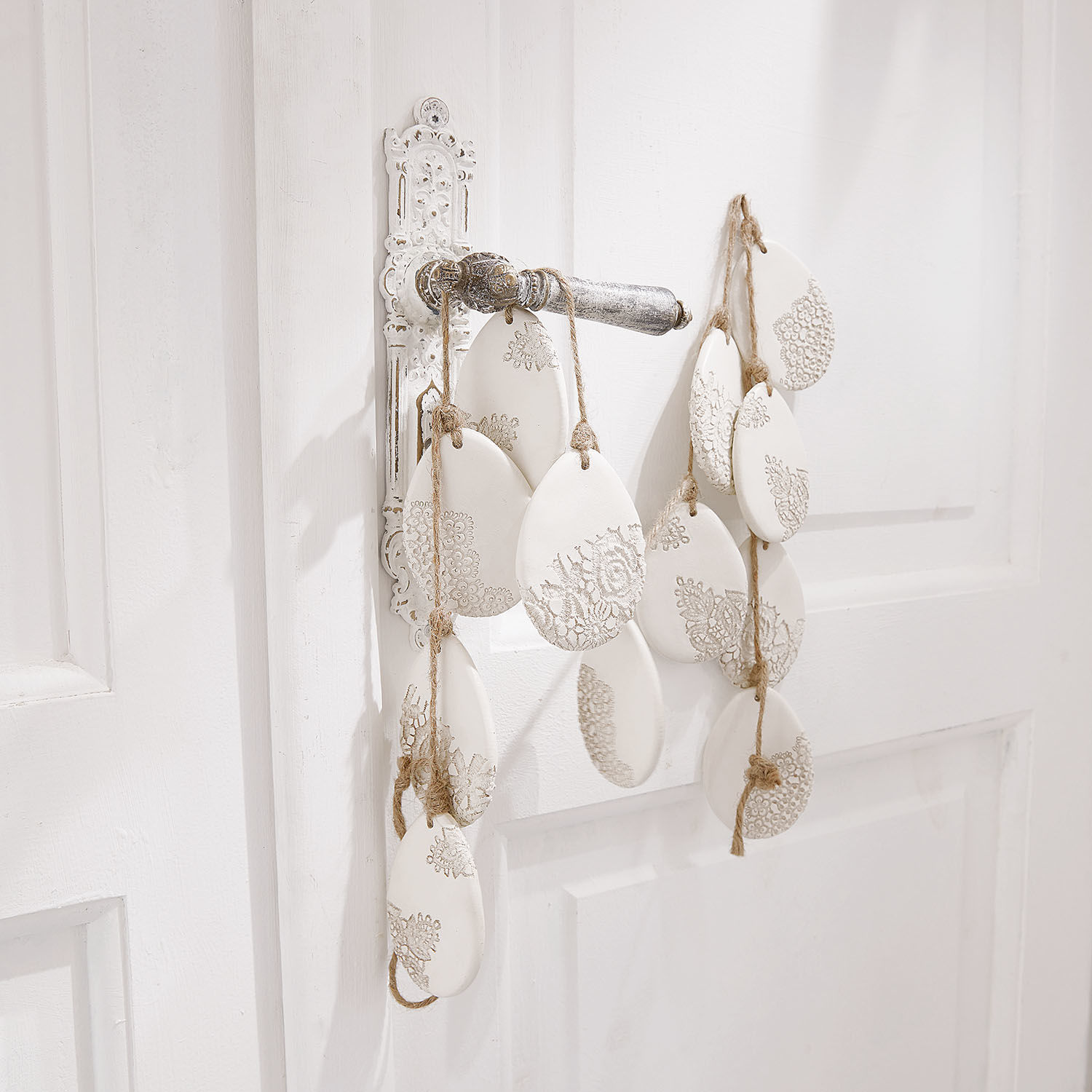 Witte keramische hangers met kantpatroon aan touw aan witte deur