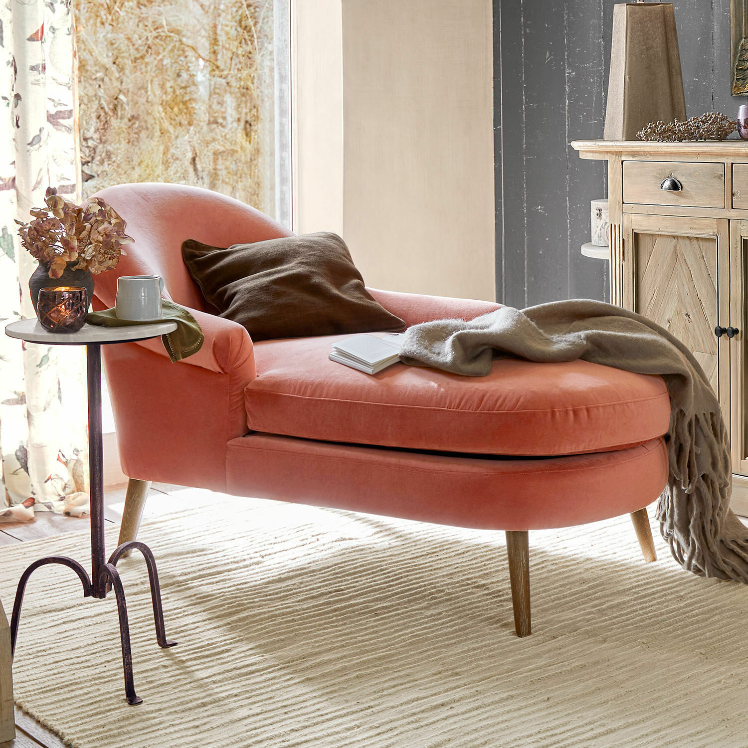 Roze fluwelen chaise longue met houten poten en bruine kussen in gezellige woonkamer