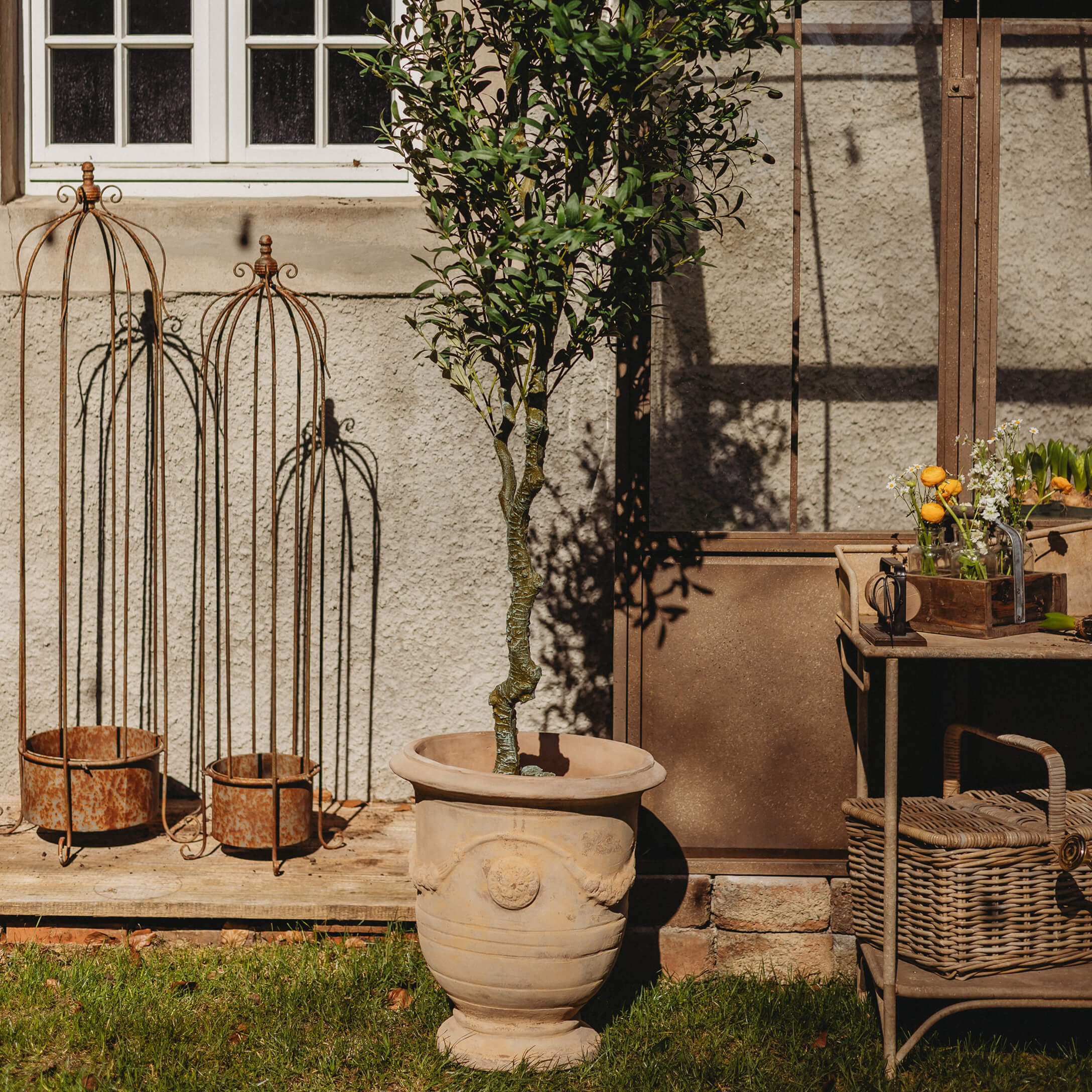 Grote beige keramische pot met groene boom in tuin met roestige metalen decoraties