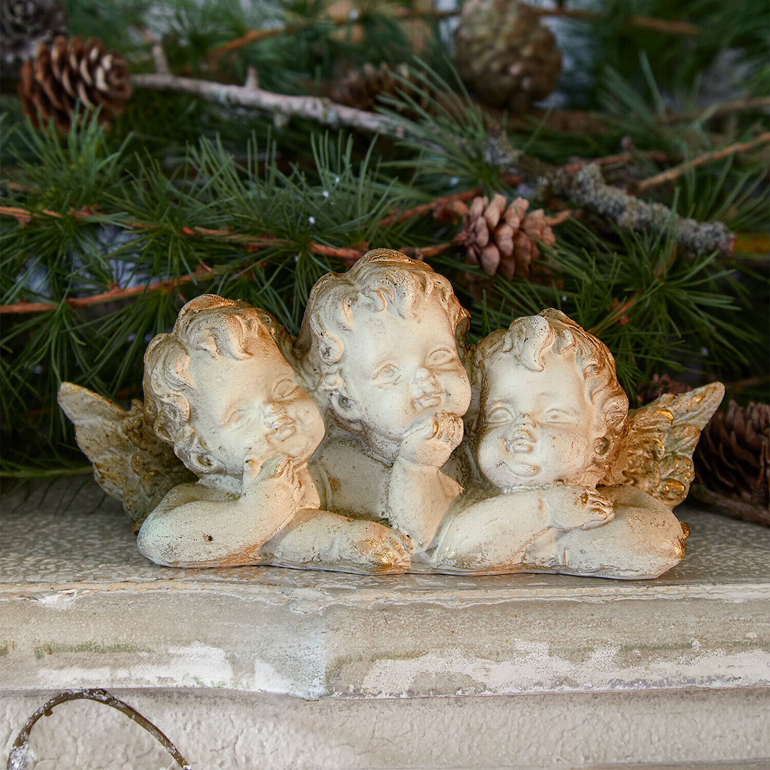 Decoratieve engelen Nivardo Beeldje van drie engelen van licht steenmateriaal met groene dennen takken op de achtergrond, feestelijke decoratie