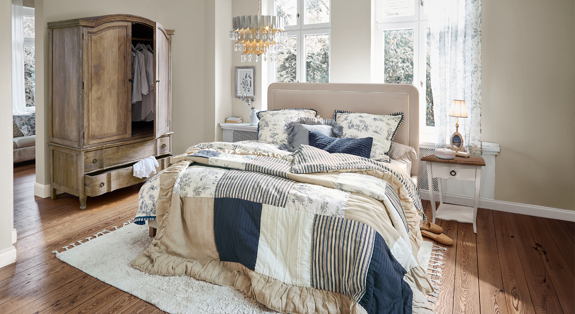 Slaapkamer met patchwork dekbed in beige, marineblauw en wit op bed met gestoffeerd hoofdeinde