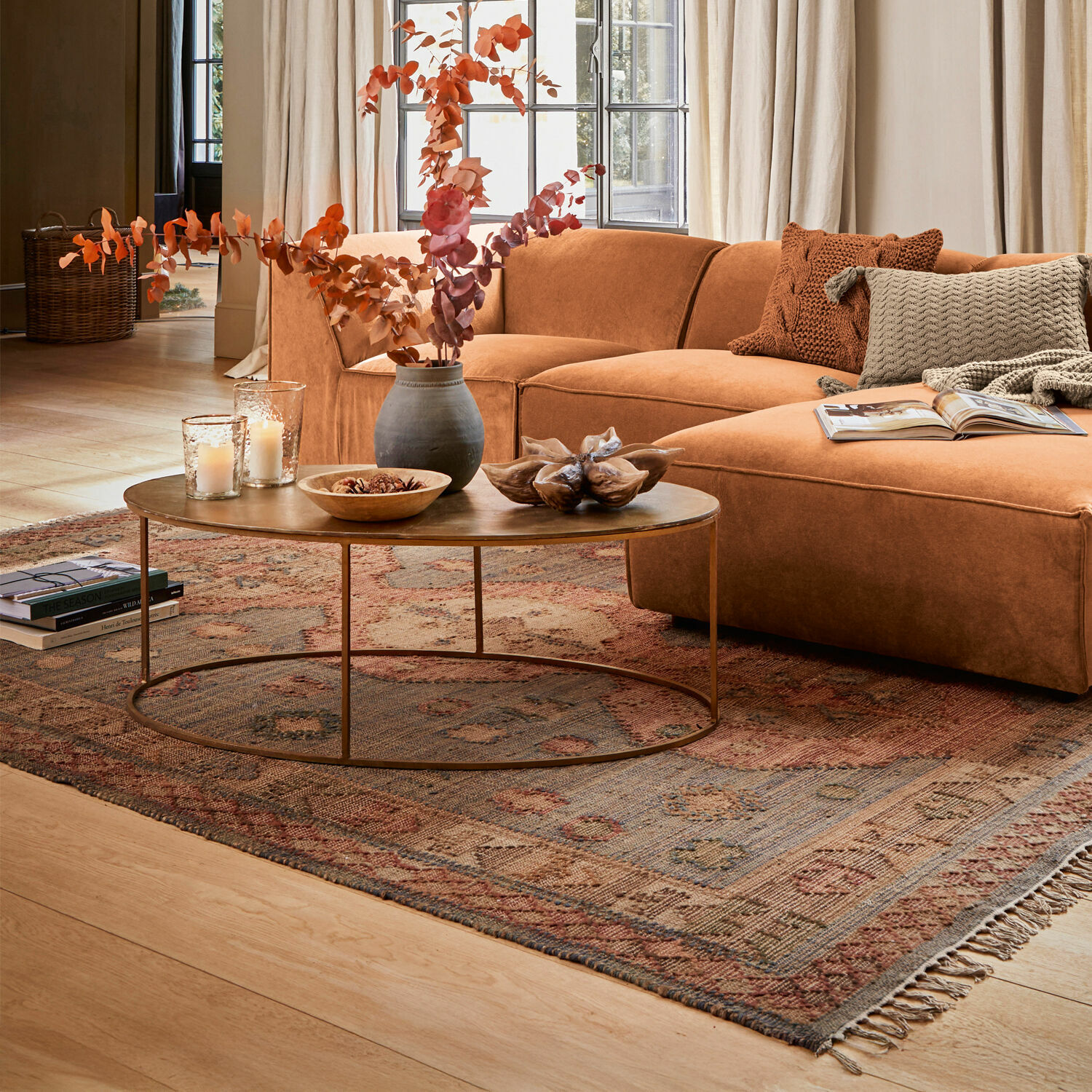 Bruine fluwelen hoekbank in lichte woonkamer met grote ramen en decoratief vloerkleed