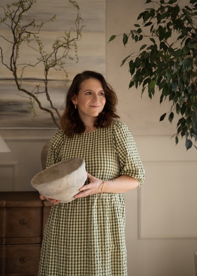Vrouw in groene geruite jurk houdt grijze keramische kom vast in een gezellige kamer