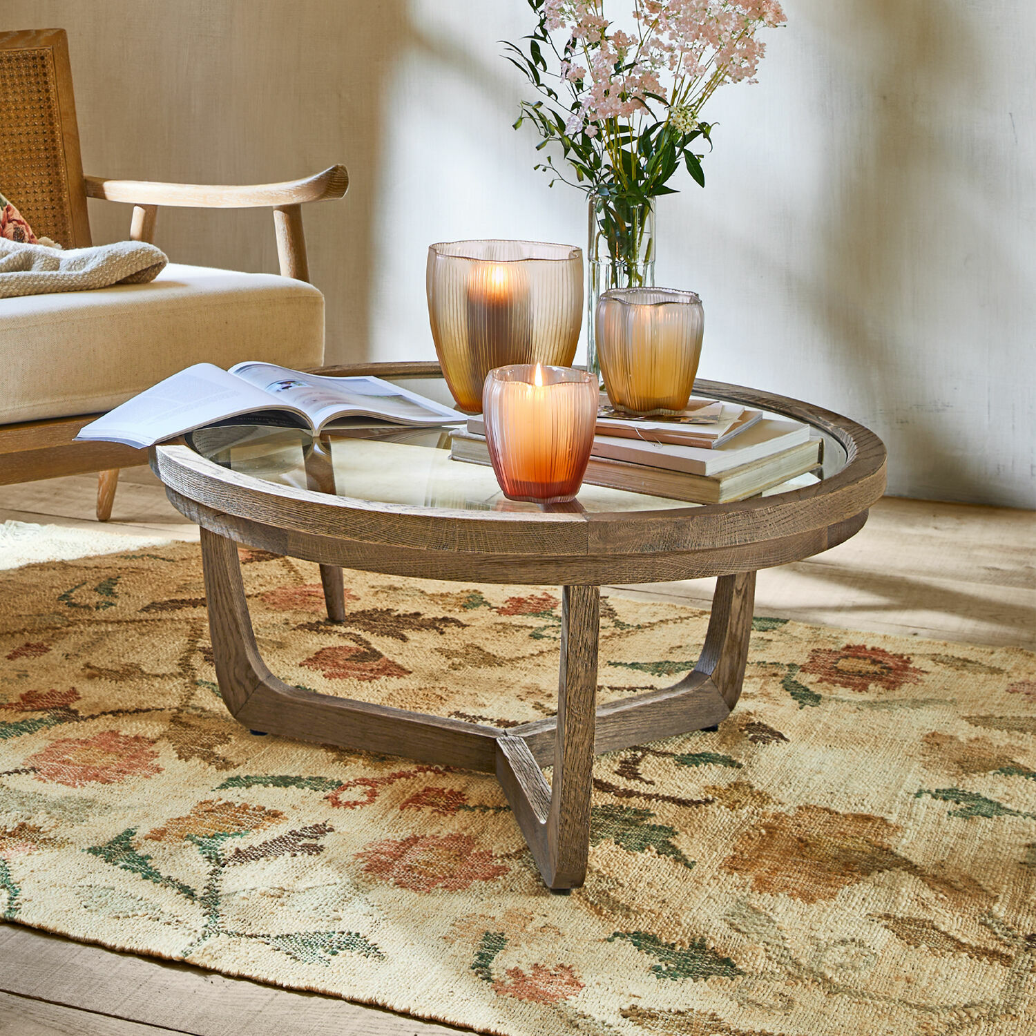 Salontafel Gradn Enclos Ronde salontafel van hout en glas op bloemenkleed met kaarsen en boeken als decoratie