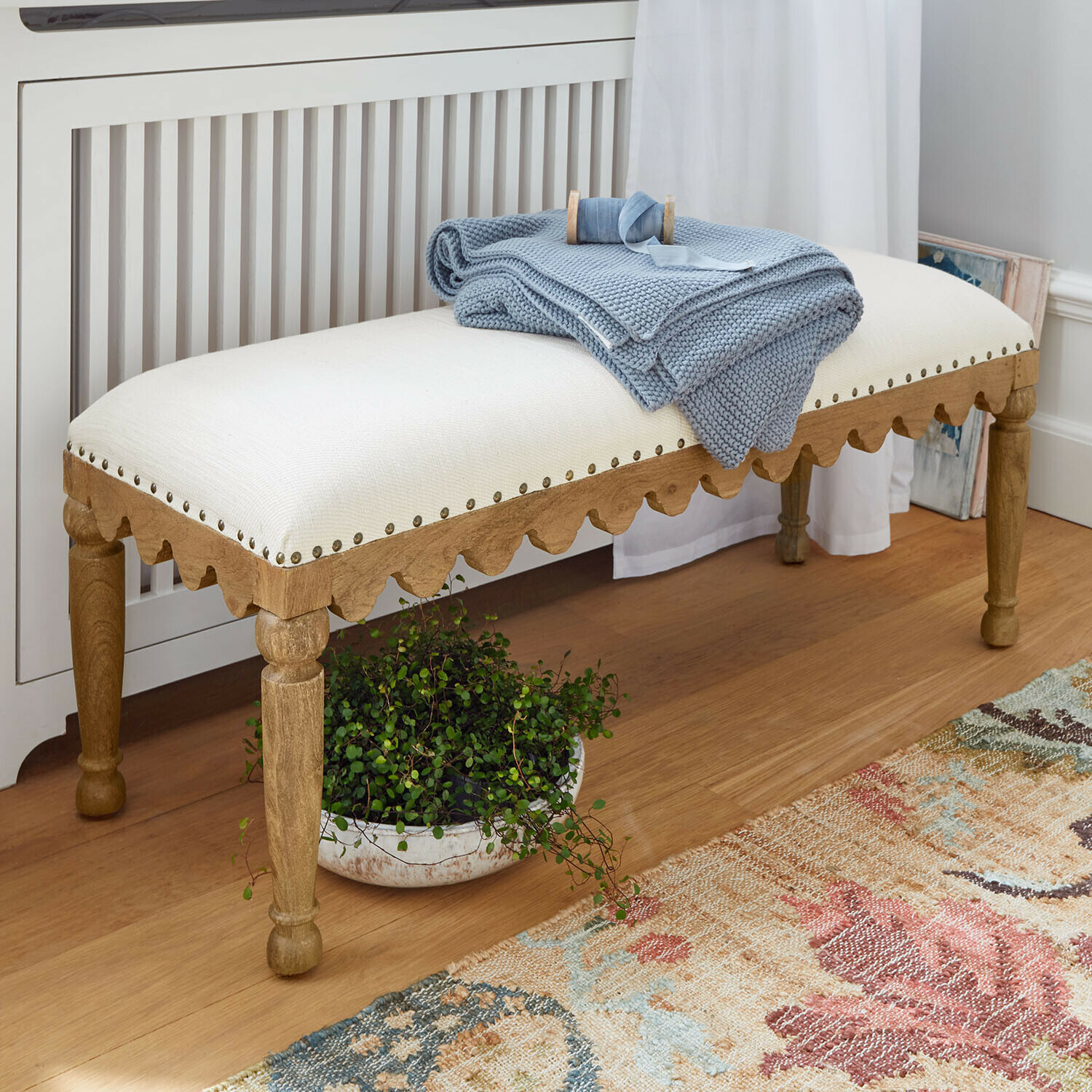 Bank van licht hout met crèmekleurige bekleding en blauwe deken in een gezellige kamer