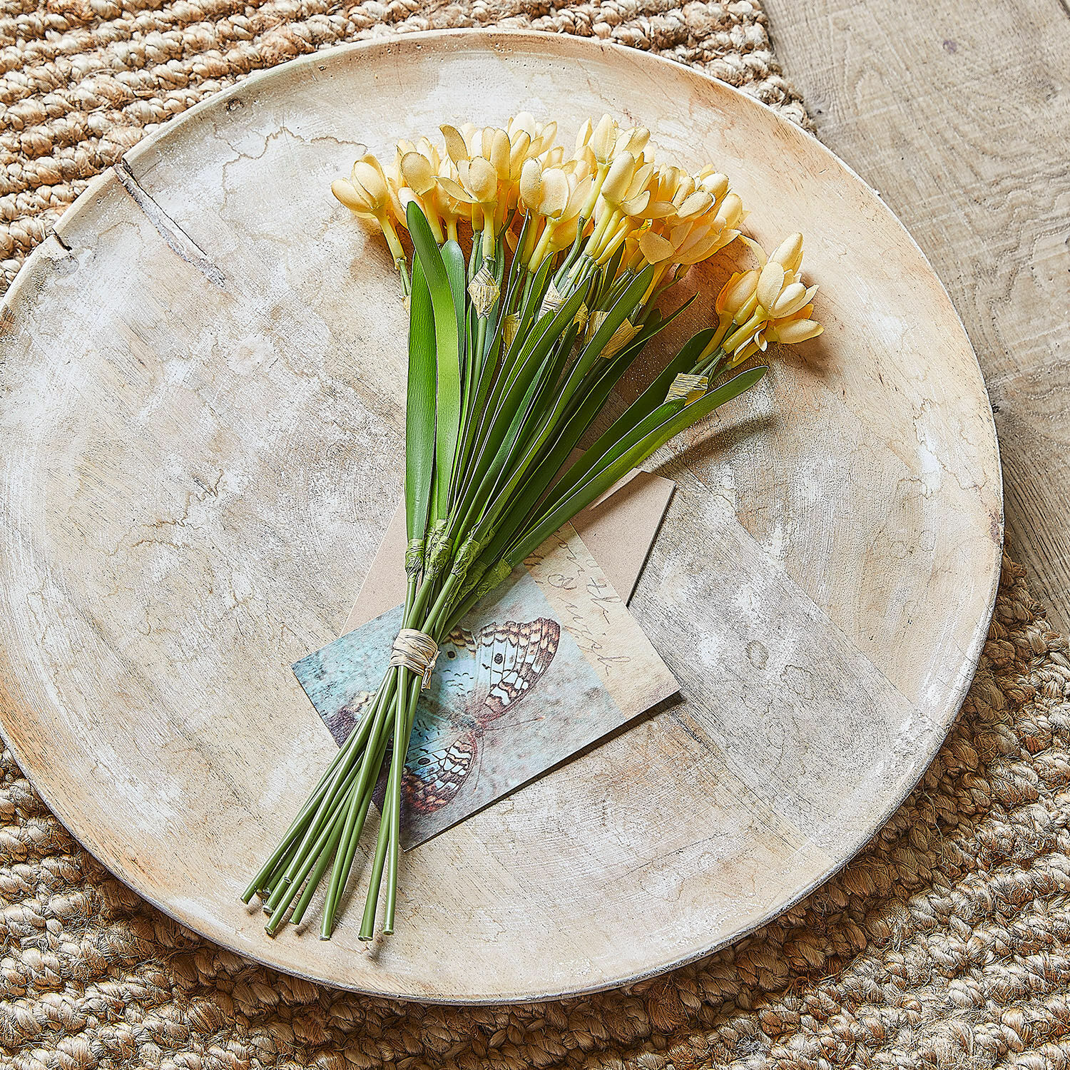 Boeket gele kunstbloemen op houten dienblad op jute vloerkleed, interieurdecoratie