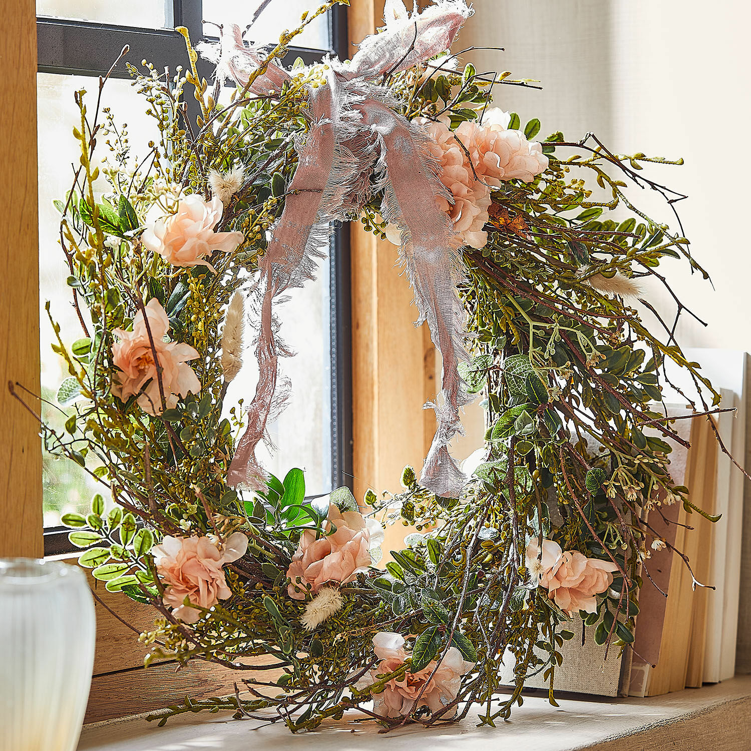 Krans Chérisse Decoratieve krans van takken, roze bloemen en groene bladeren met roze lint bij het raam