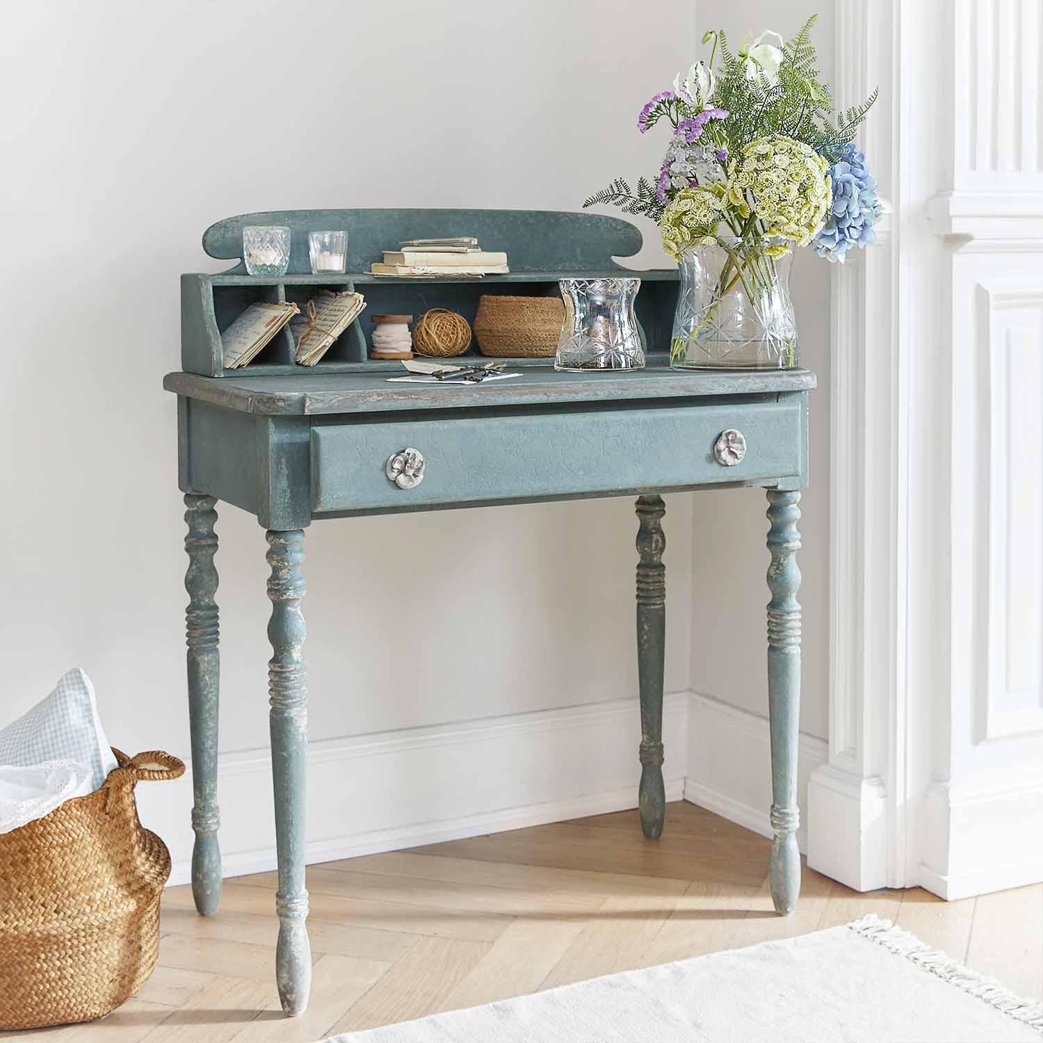 Blauw houten bureau met lade en vakken, versierd met bloemenvaas en kaarsen