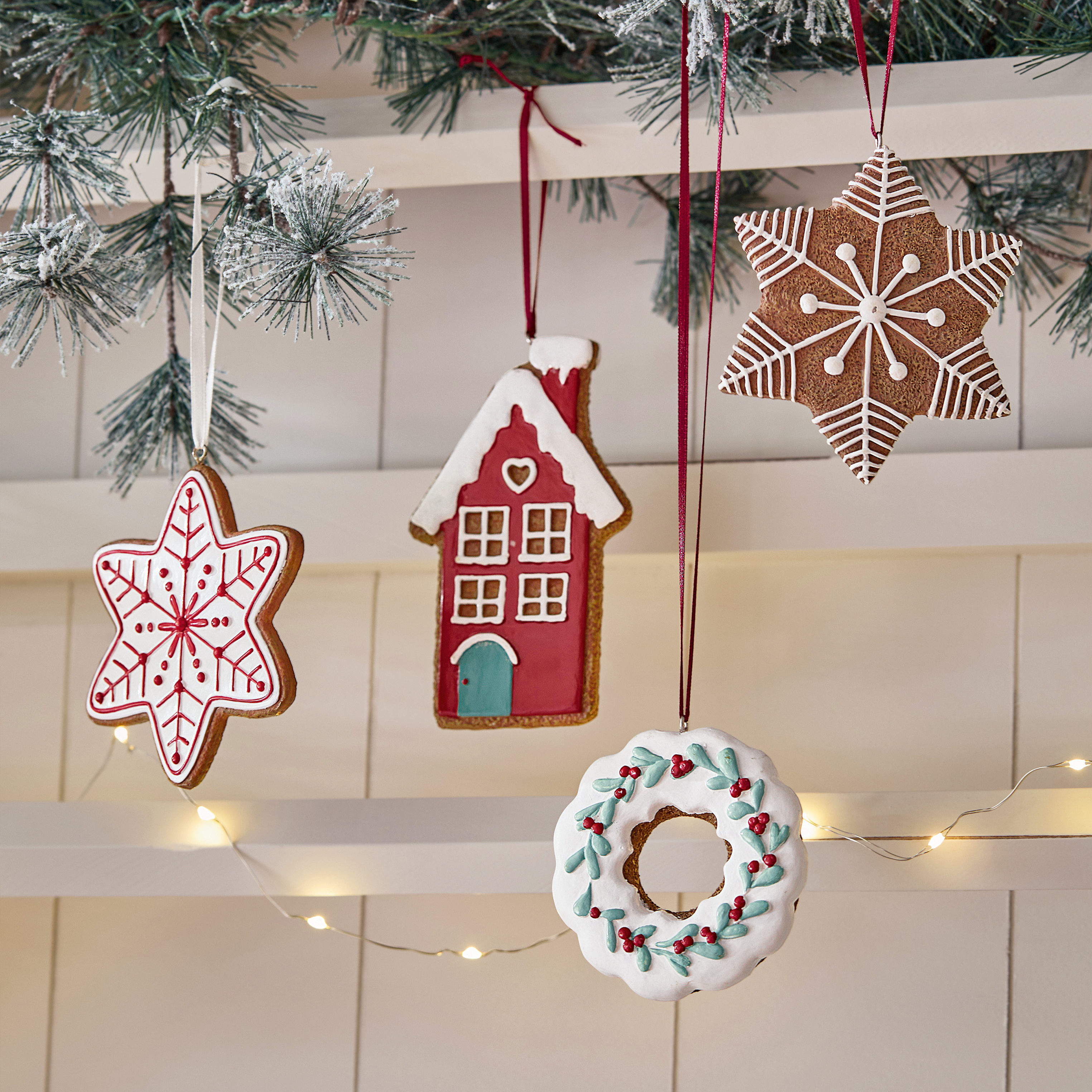 Kerstversieringen van peperkoek in ster-, huis- en kransvorm met gekleurde glazuur aan dennentak