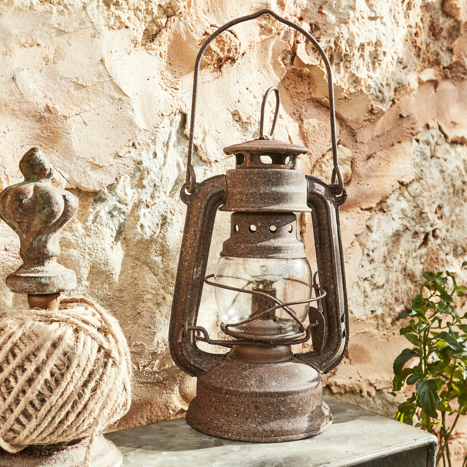 Rustieke metalen olielamp met roestkleurige afwerking tegen een stenen muur, vintage decoratie