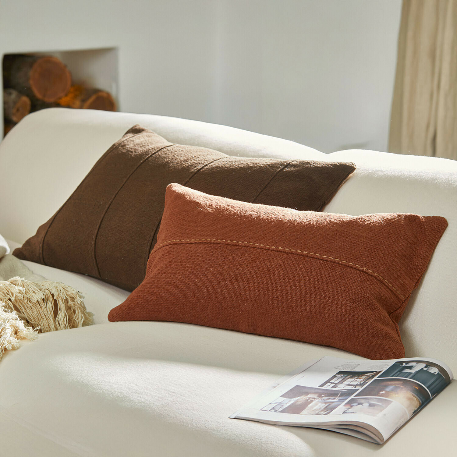 Bruine en baksteenrode sierkussens op een witte bank met tijdschrift ernaast, woontextiel