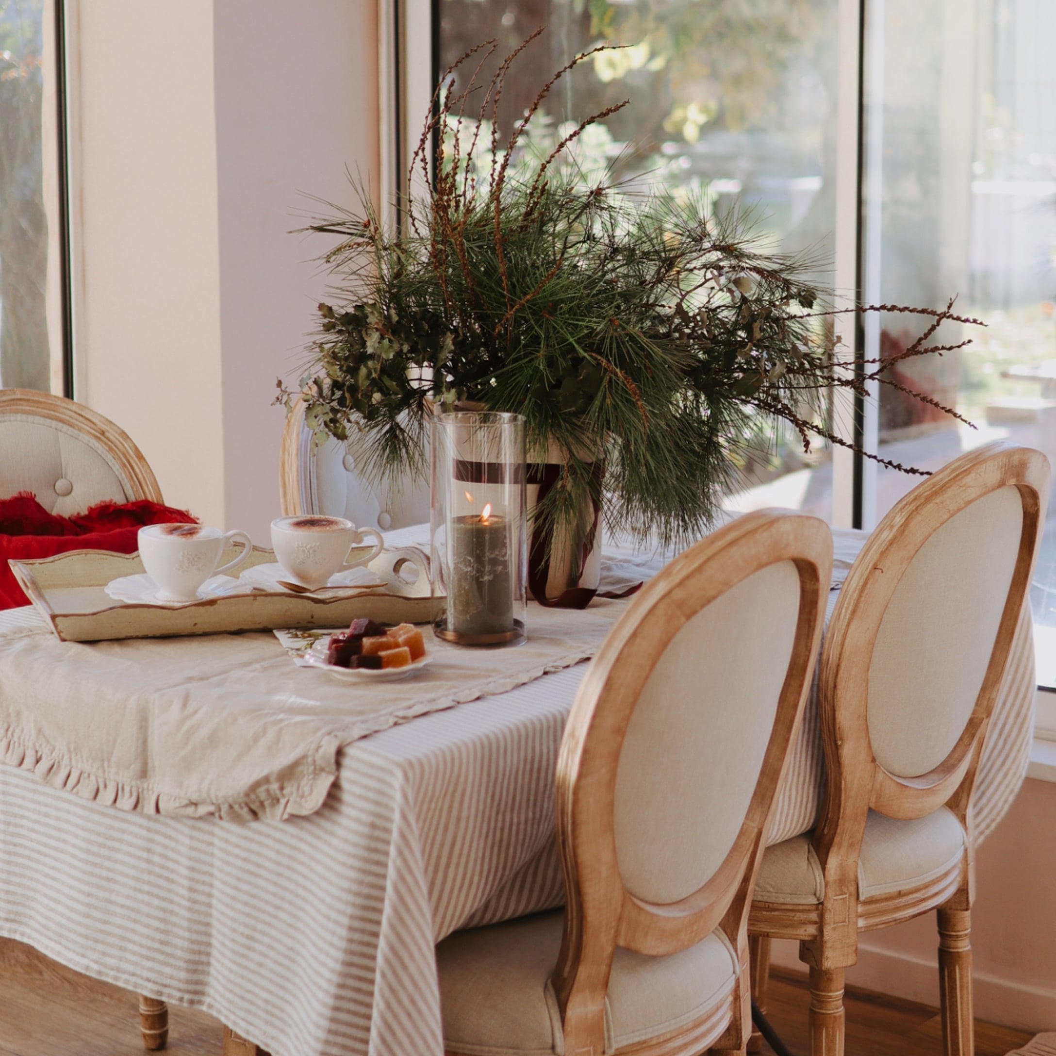 Gezellige tafel met beige tafelkleed, houten stoelen en kerstdecoratie van groene takken