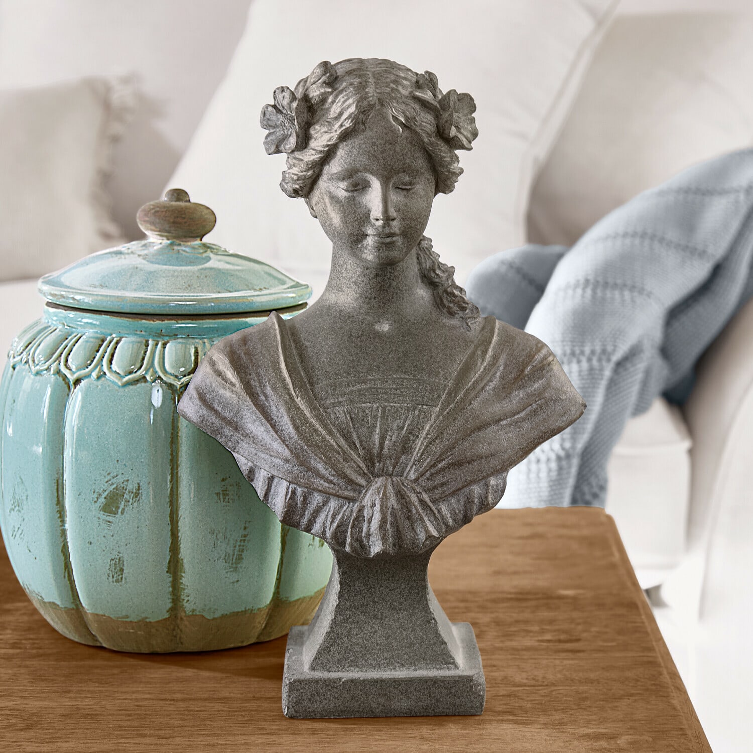 Buste Alexandra Grijs stenen vrouwenbuste met bloemen in het haar op houten tafel naast turquoise keramische pot