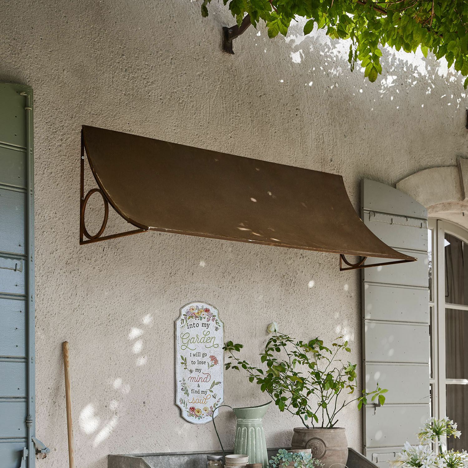 Bruine metalen wandluifel boven raam met tuindecoratie en plant in pot