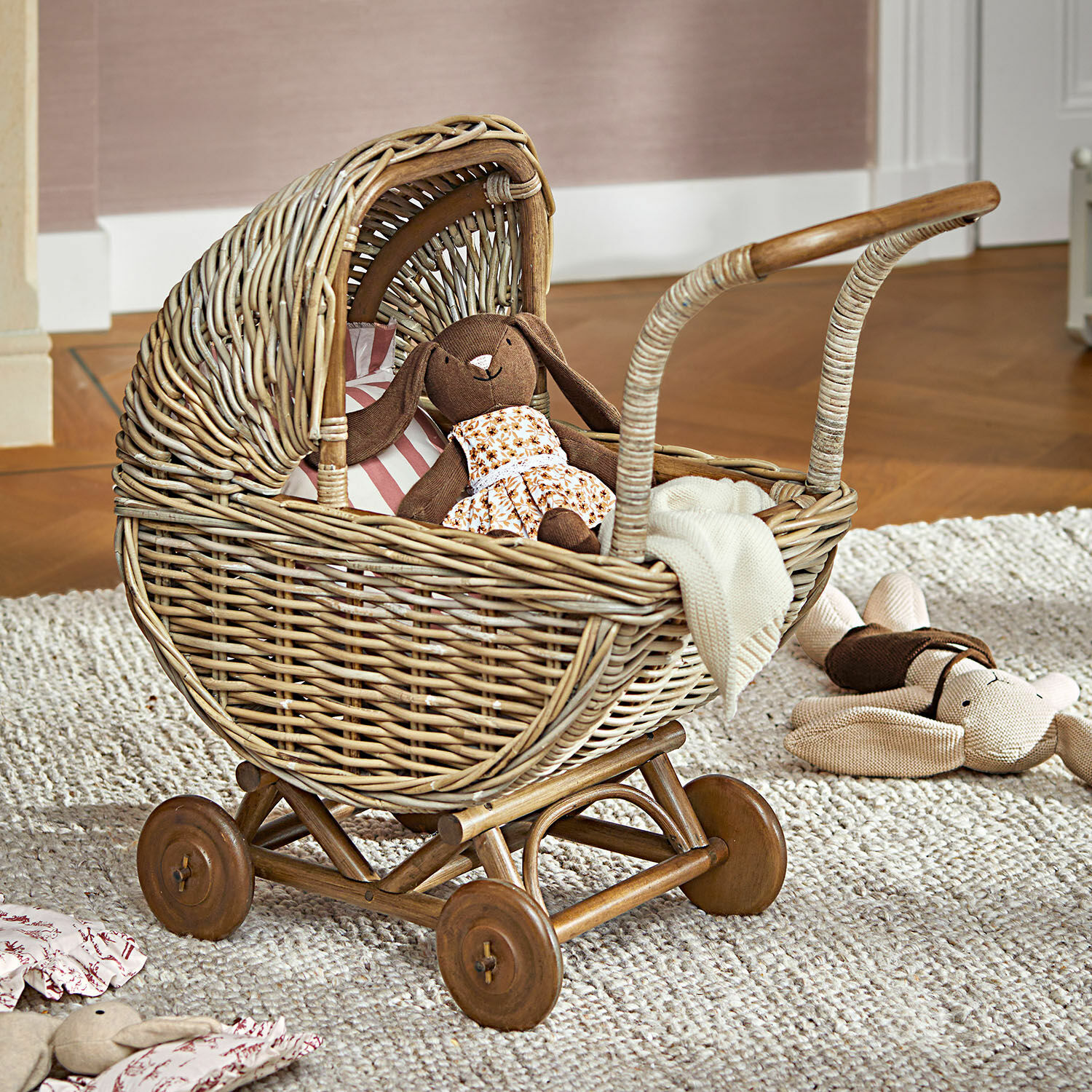 Poppenwagen Fableton Rieten kinderwagen met houten wielen en knuffels op een vloerkleed in een kinderkamer