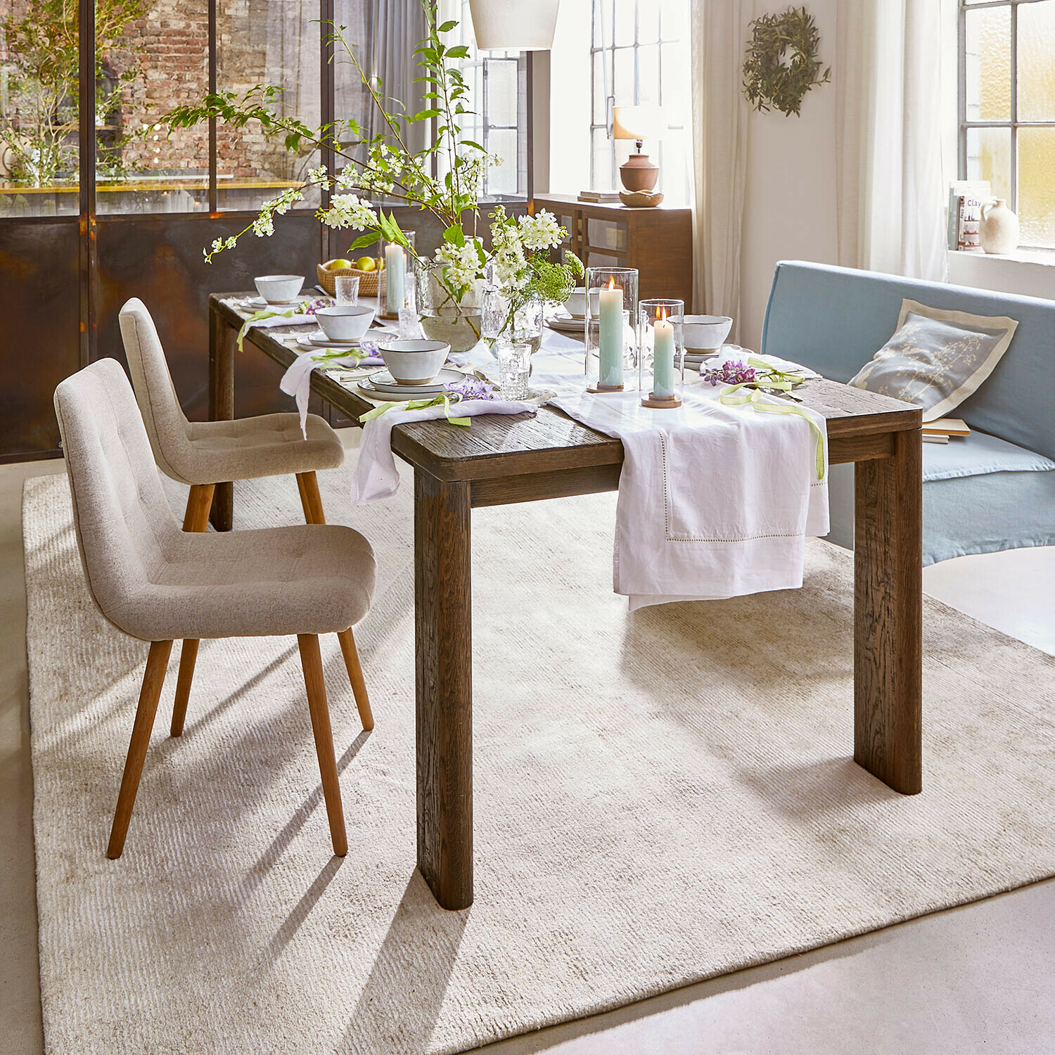 Rustieke eettafel van donker hout met wit tafelkleed en kaarsen in lichte woonkamer