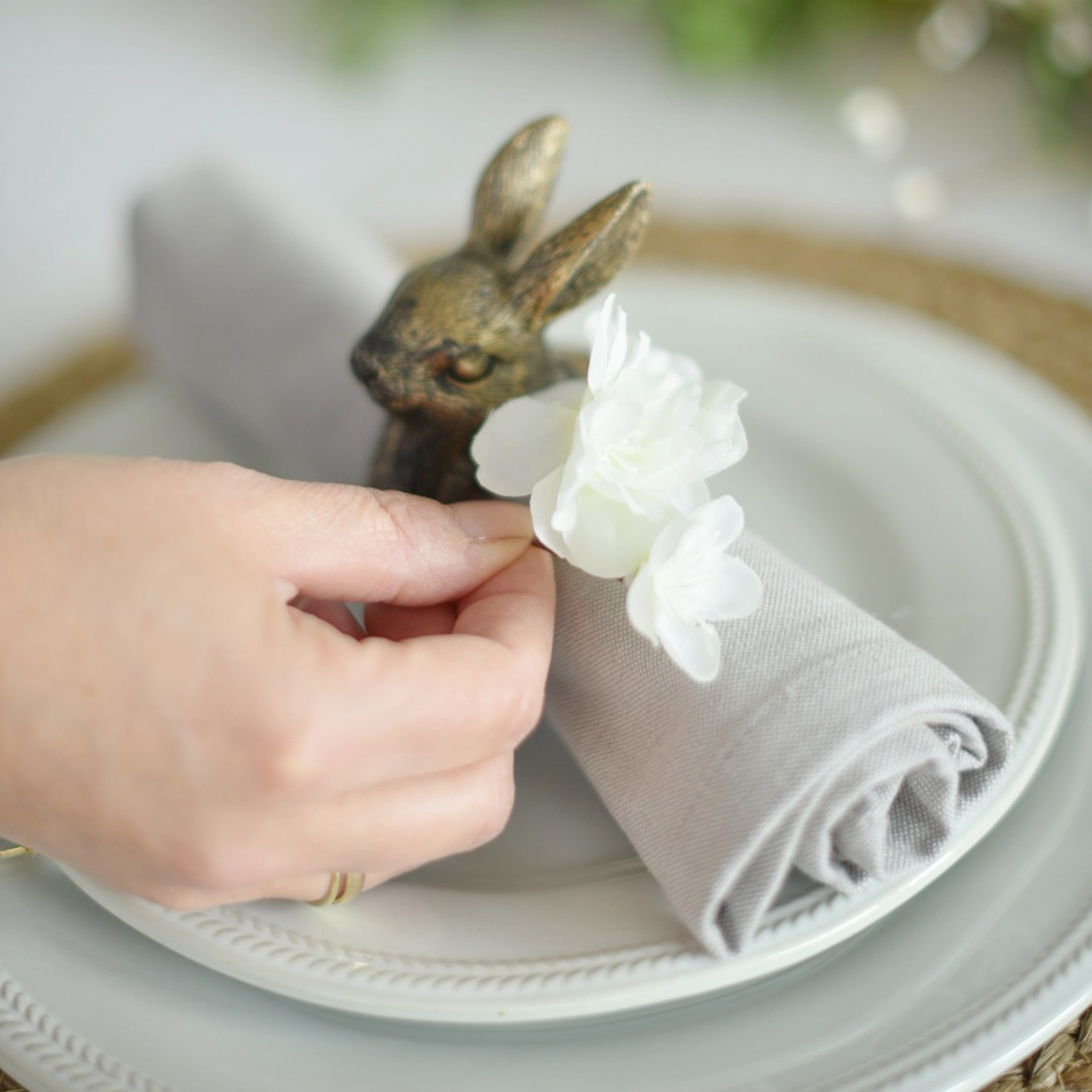 Grijze linnen servetring met witte bloem en messing konijn decoratie op wit bord