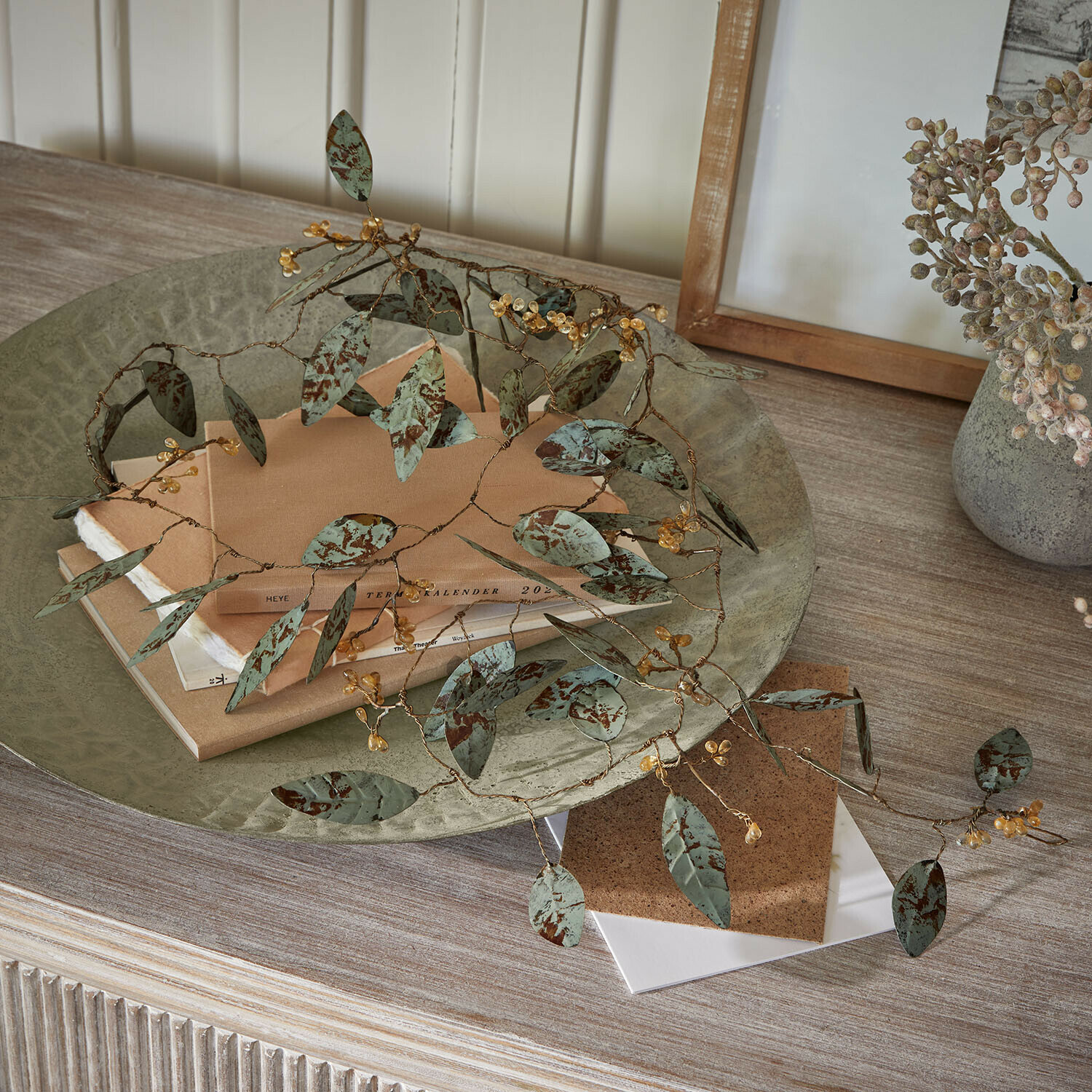Decoratieve metalen tak met groene bladeren en gele bessen op houten tafel met boeken