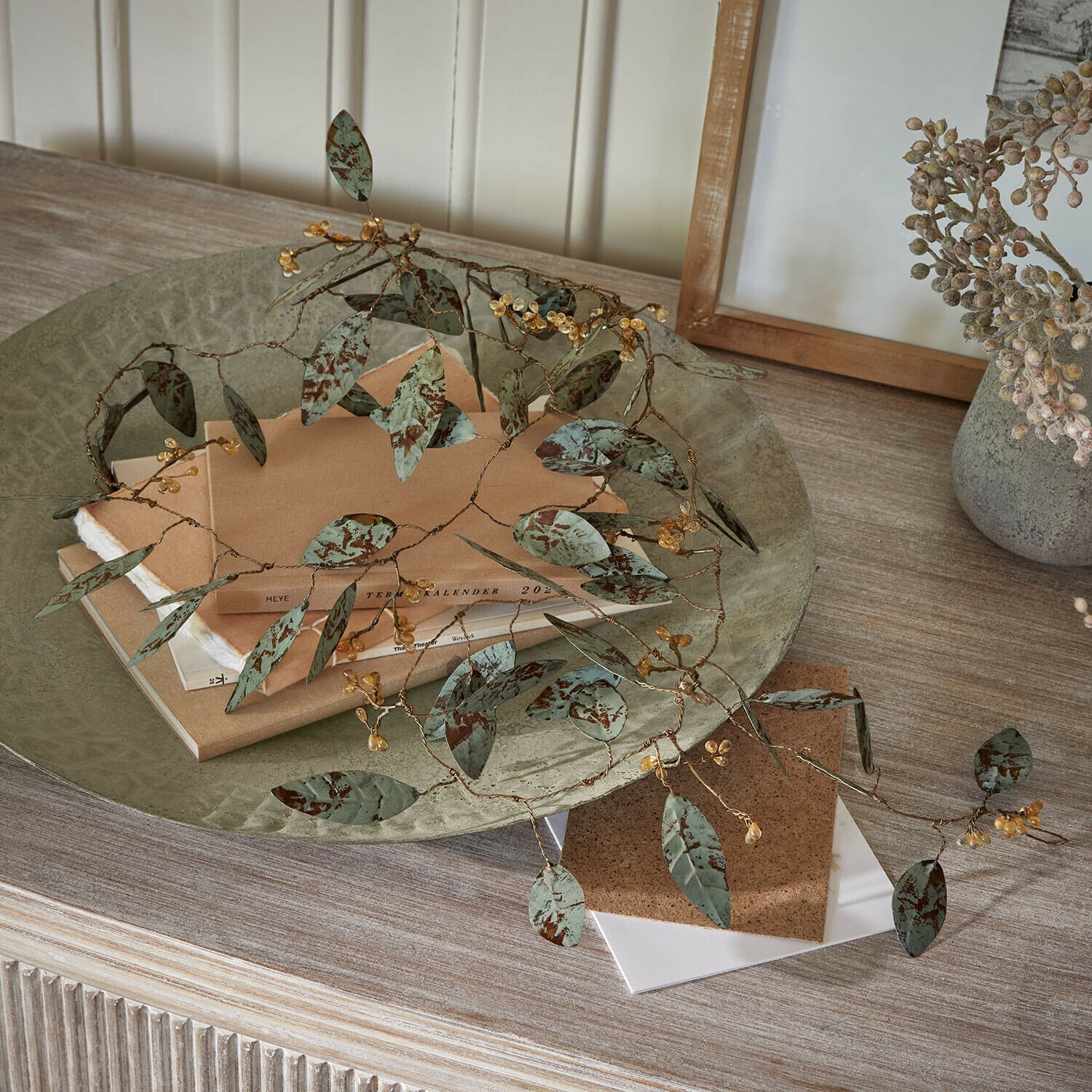 Guirlande Florivine Decoratieve metalen tak met groene bladeren en gele bessen op houten tafel met boeken
