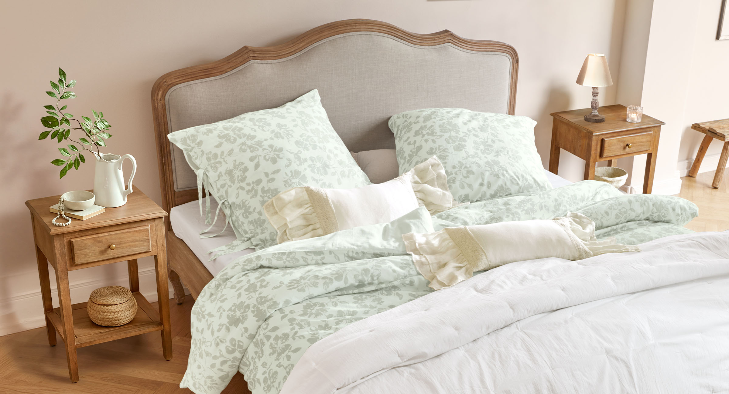 Bed met houten hoofdbord en licht bloemenpatroon beddengoed, houten nachtkastjes met lamp en decoratie