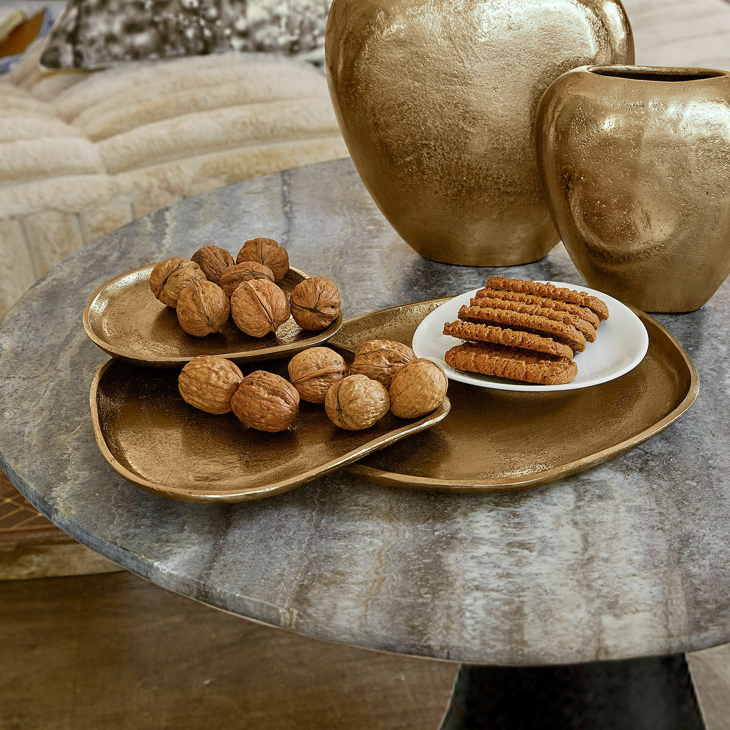 Set gouden metalen schalen en vazen op marmeren tafel met noten en koekjes