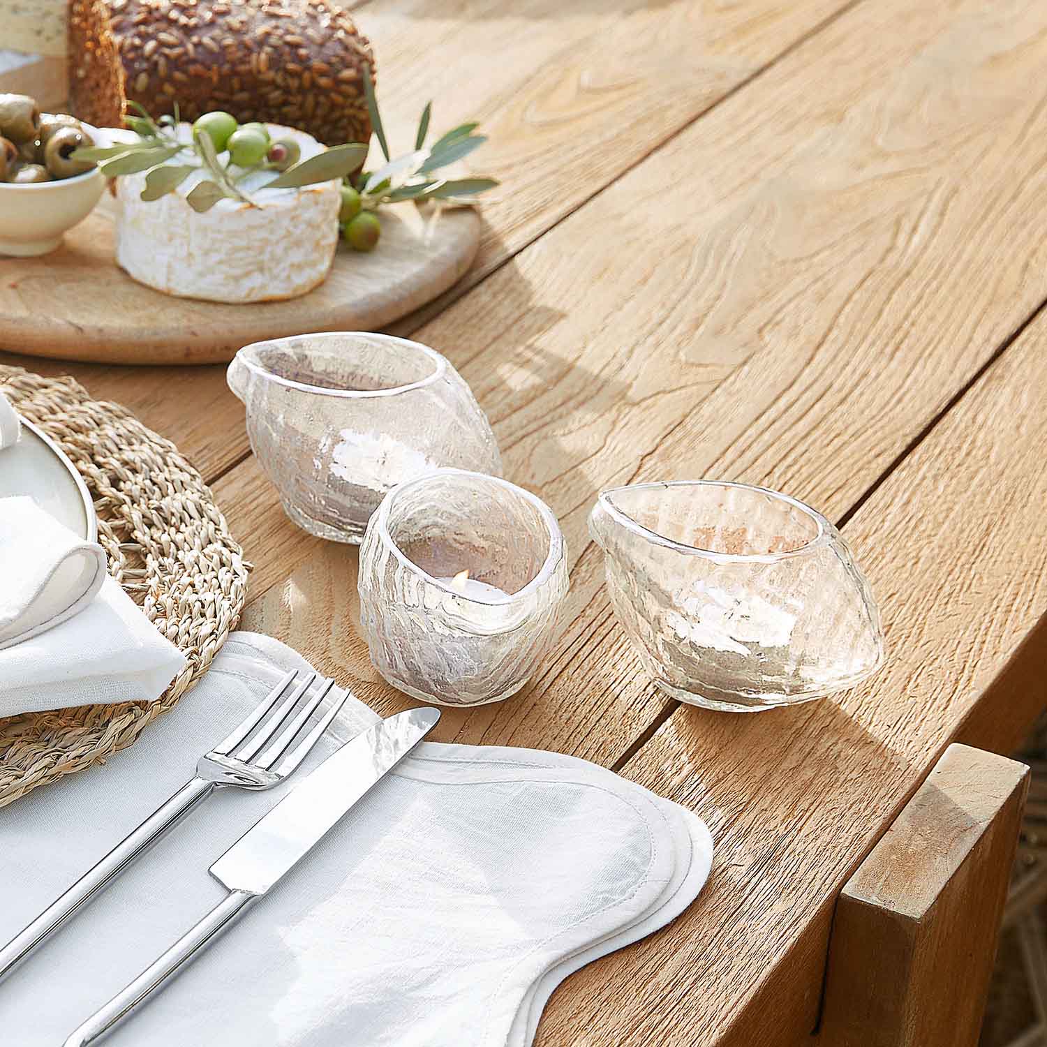 Set van drie doorzichtige glazen theelichthouders met onregelmatige vorm op een lichte houten tafel