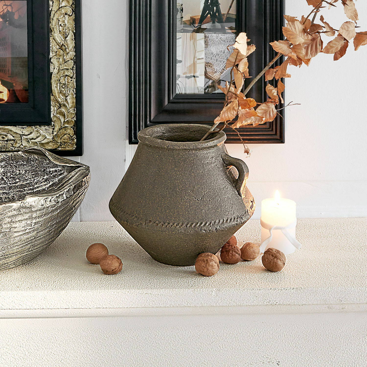 Bruine keramische vaas met handvat en droge bladeren, tafeldecoratie met noten en kaars