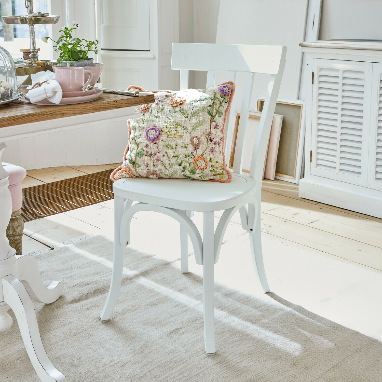 Witte houten stoel met geborduurd bloemenkussen in lichte, gezellige eetkamer
