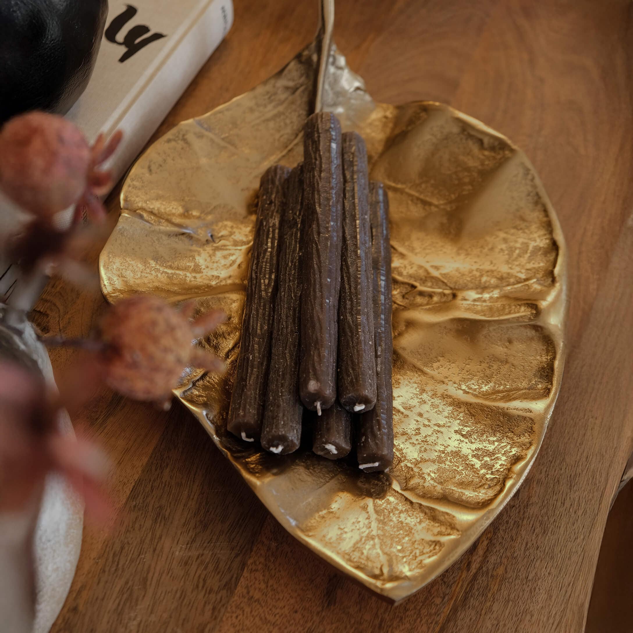 Gouden metalen schaal in bladvorm met bruine decoratieve kaarsen op houten tafel