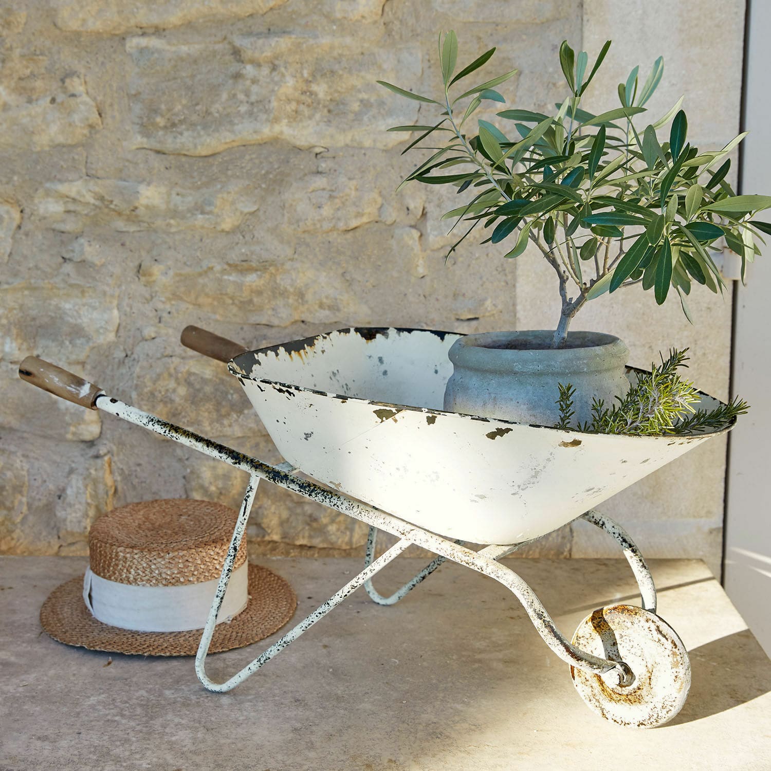 Sierkruiwagen Padoux Witte metalen kruiwagen met verweerde look, pot en groene planten voor stenen muur