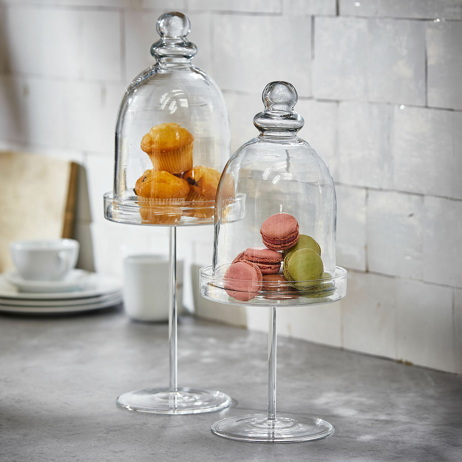 Glazen standaards met doorzichtige stolpen met muffins en macarons op een keukenblad