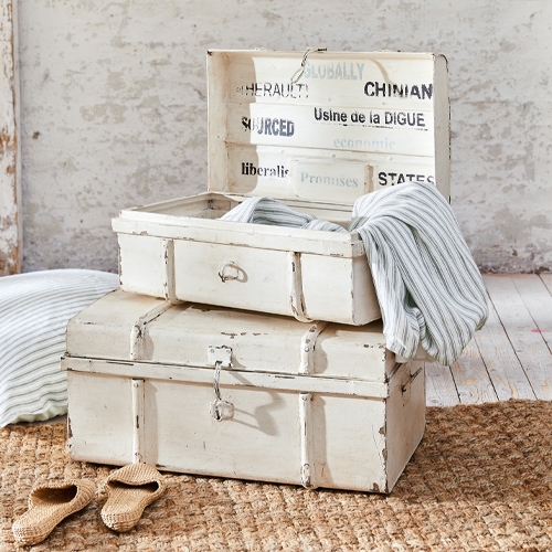 Witte houten vintage kisten met textiel en sloffen op een jute vloerkleed
