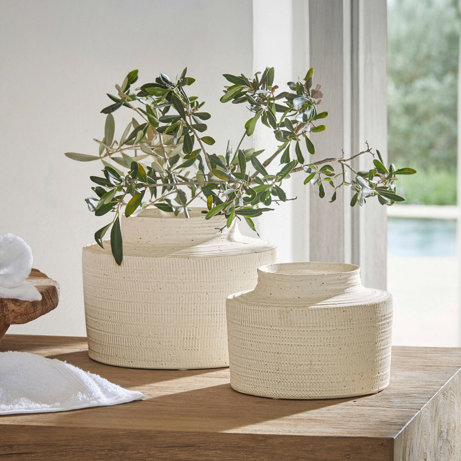 Twee crèmekleurige keramische vazen met structuur op houten tafel met groene takken