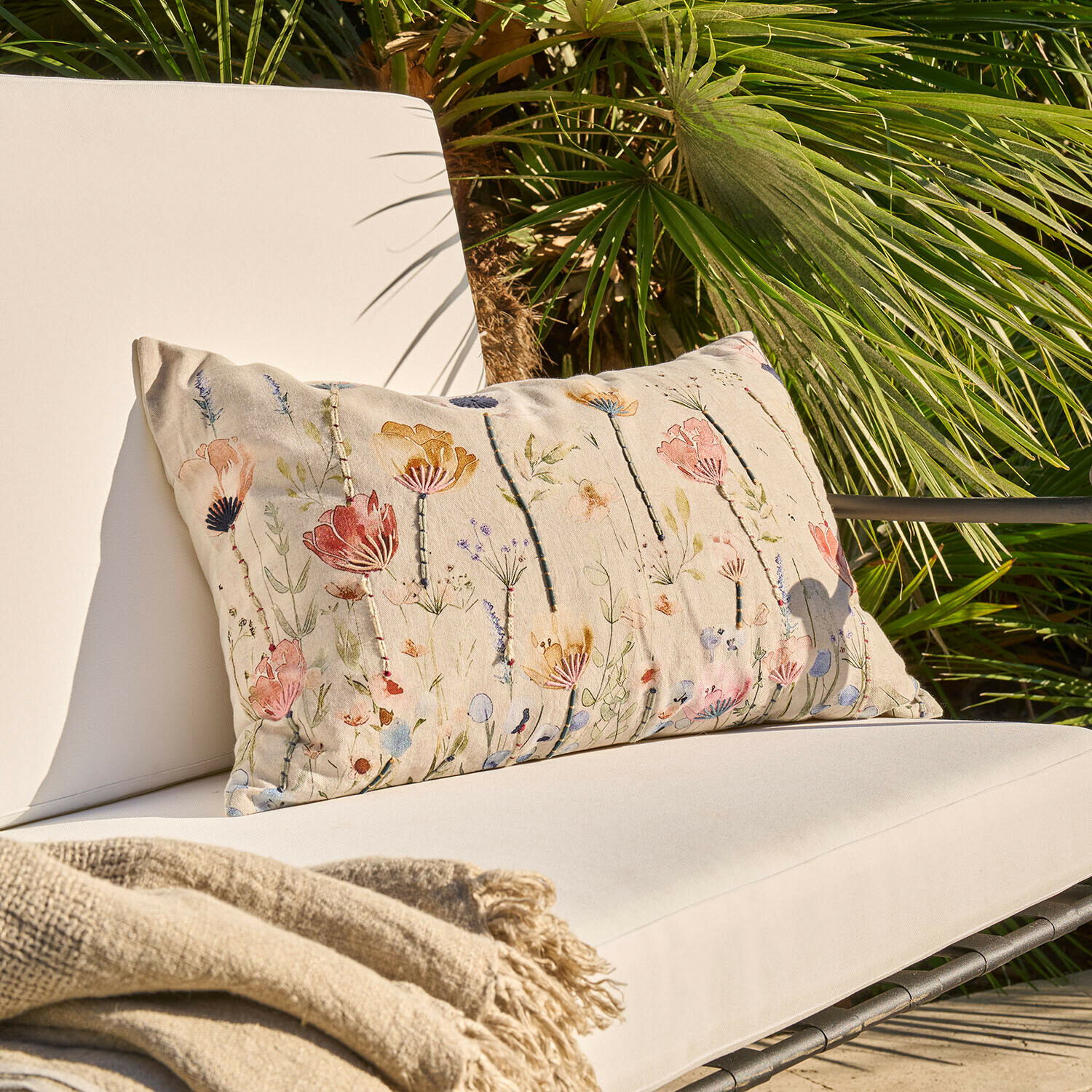 Kussenhoes Cadrinela Beige sierkussen met bloemenpatroon op lichte tuinstoel met beige deken